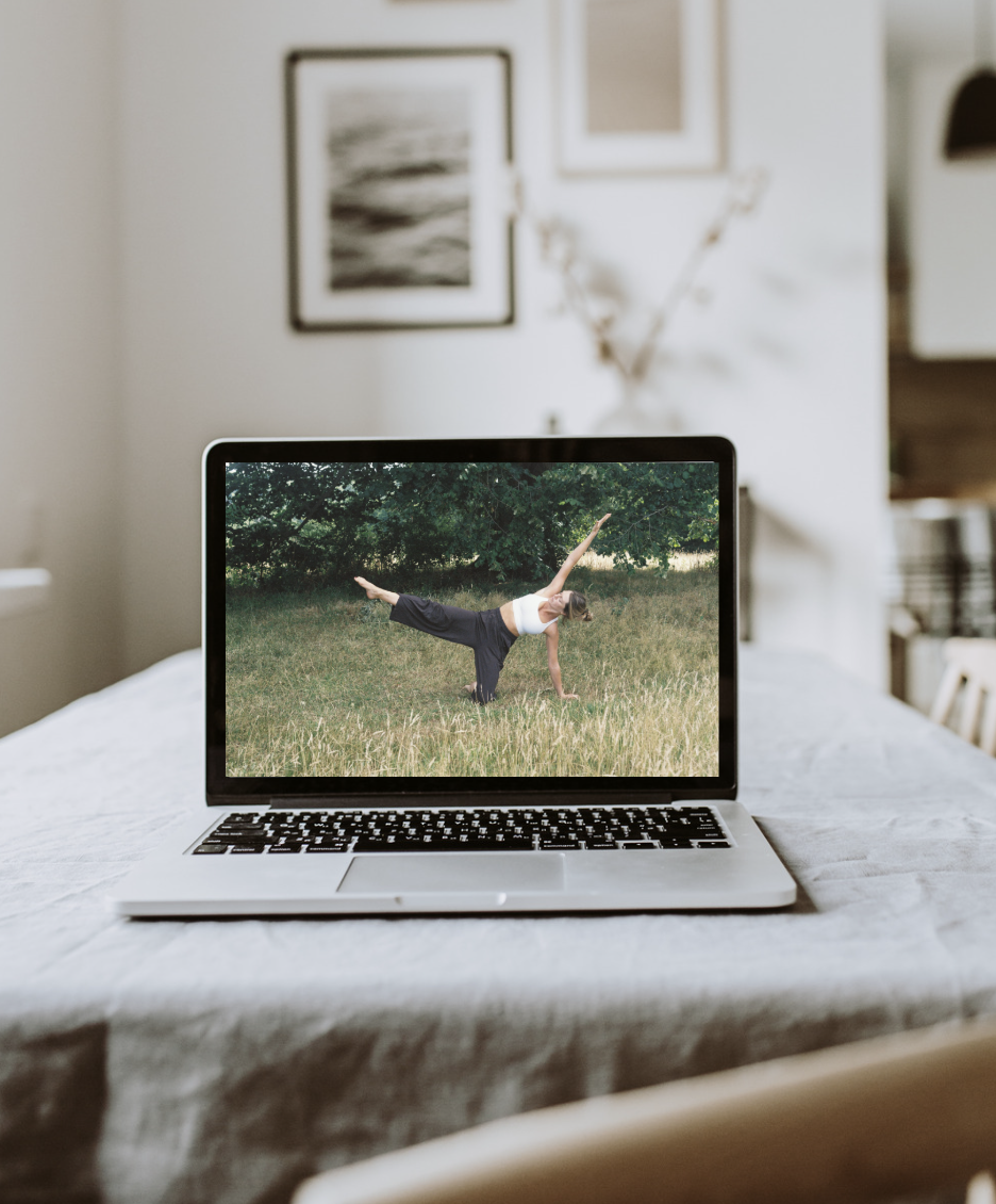 Laptop on a table displaying a woman doing yoga outdoors in a grassy area with trees.