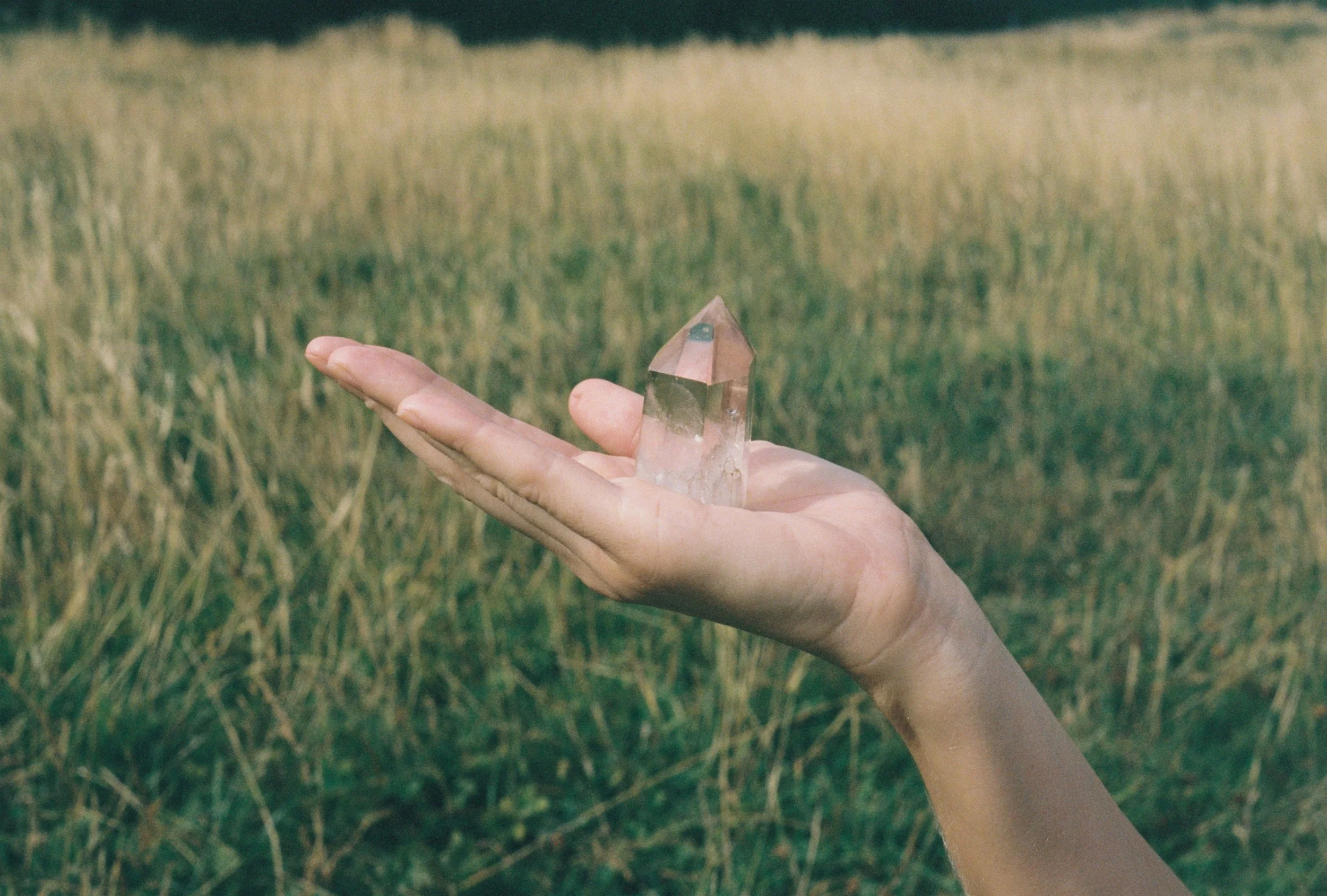 A person's hand holding a pyramid-shaped crystal in a grassy outdoor setting.