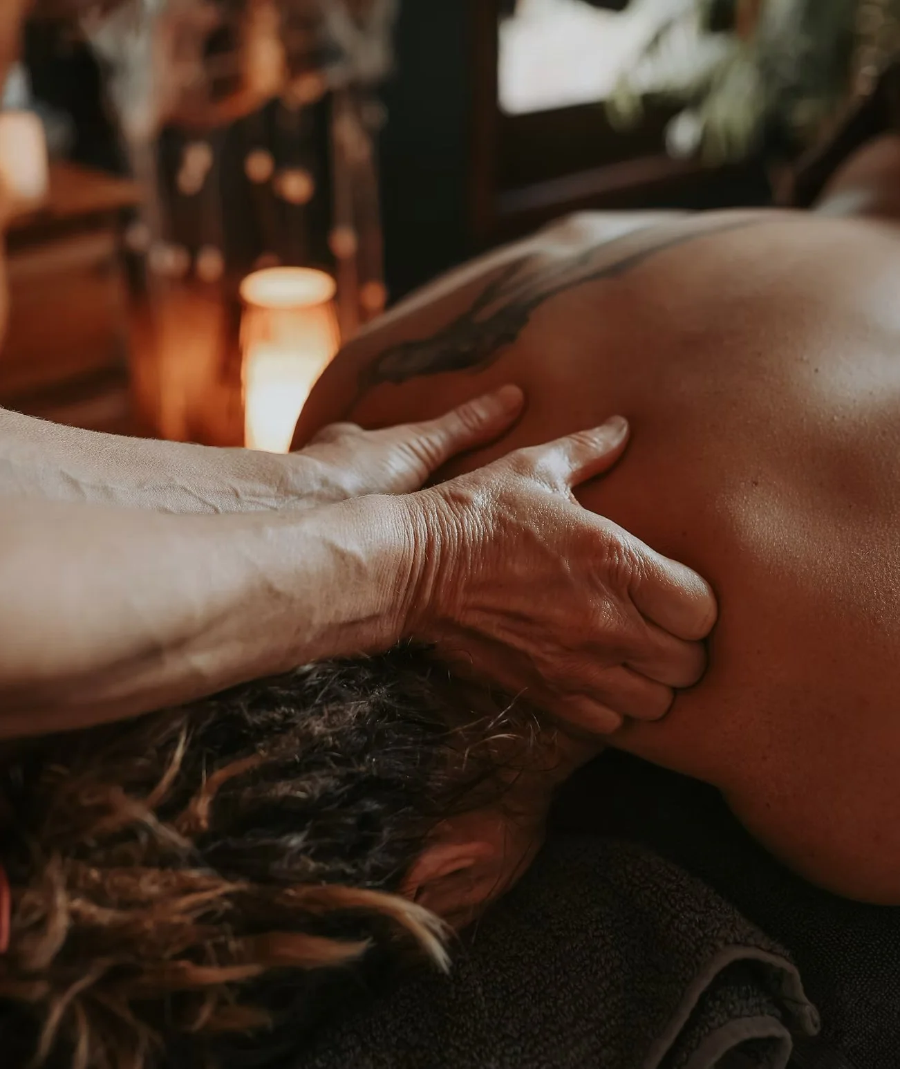 Gina is massaging the shoulders of someone who is laying down. It's in a relaxing and calm environment.