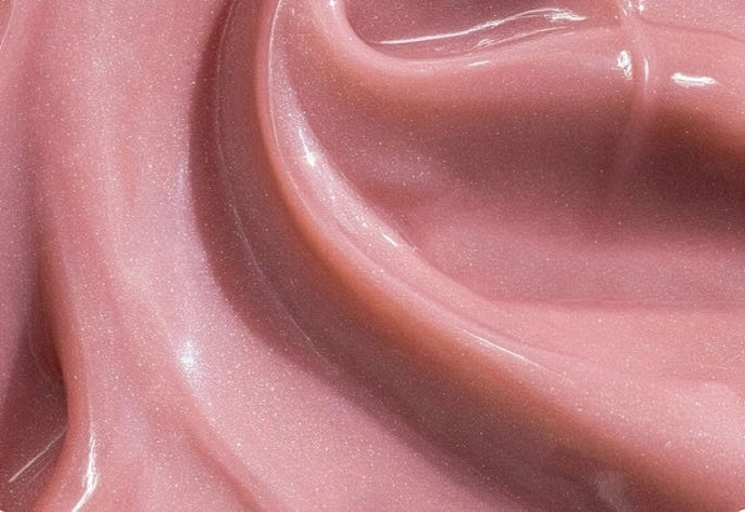 Close-up of pink, shiny lipgloss swatch with sparkling highlights.