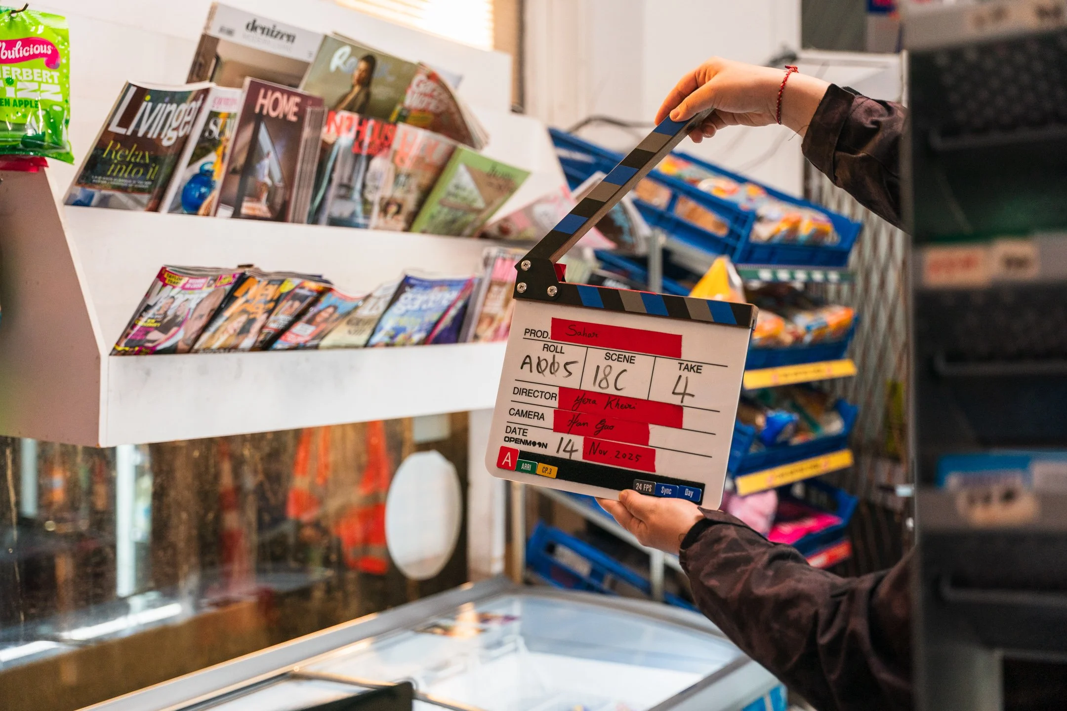 A person holding a film clapperboard in front of a magazine display at a store.