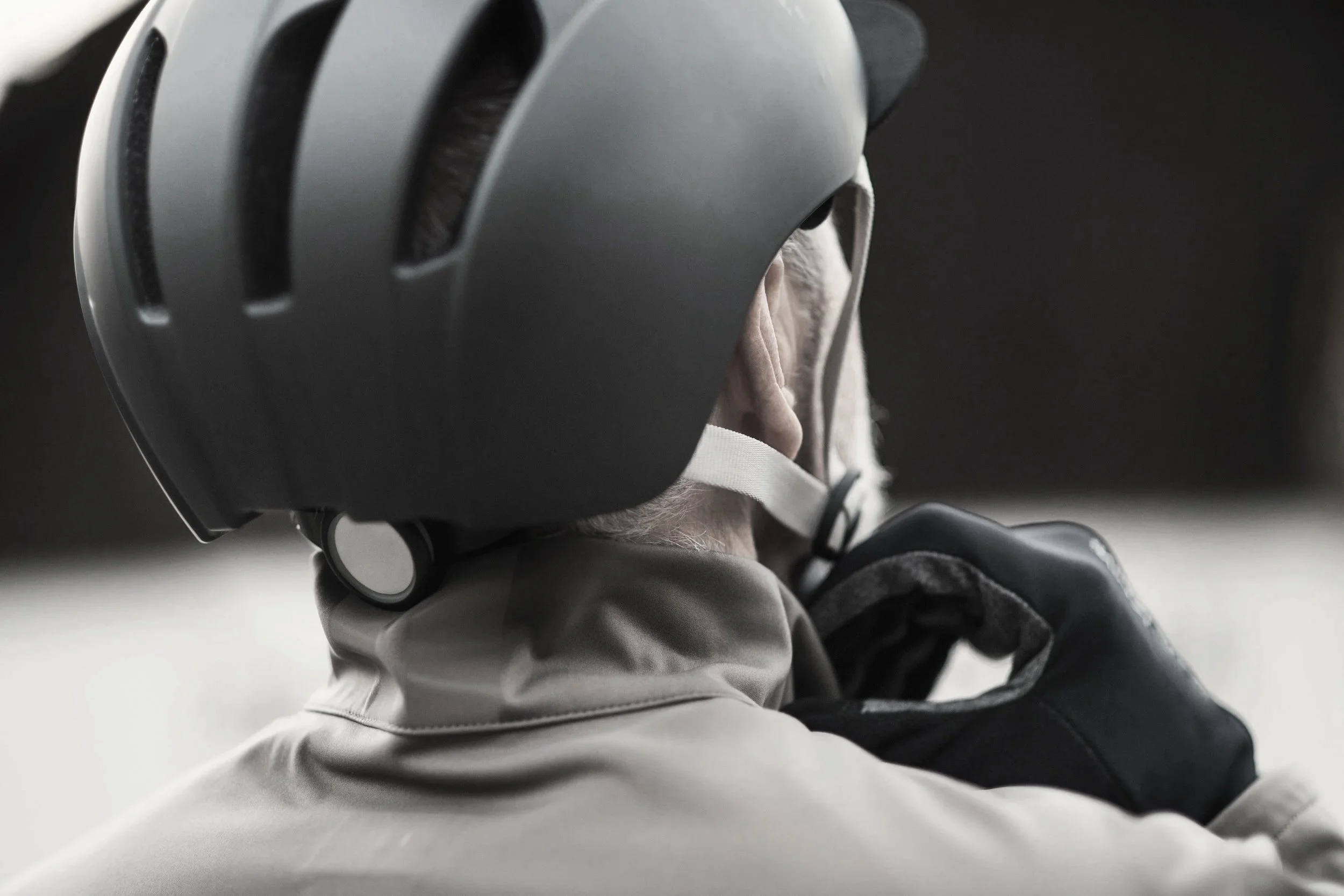 Close-up of a person in a gray helmet and jacket, riding a bicycle, with their hand to their face.