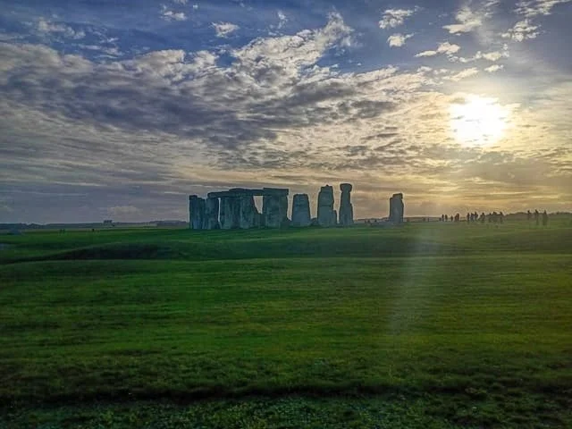 Sunset view of Stonehenge on a grassy plain with clouds and scattered trees in the background
