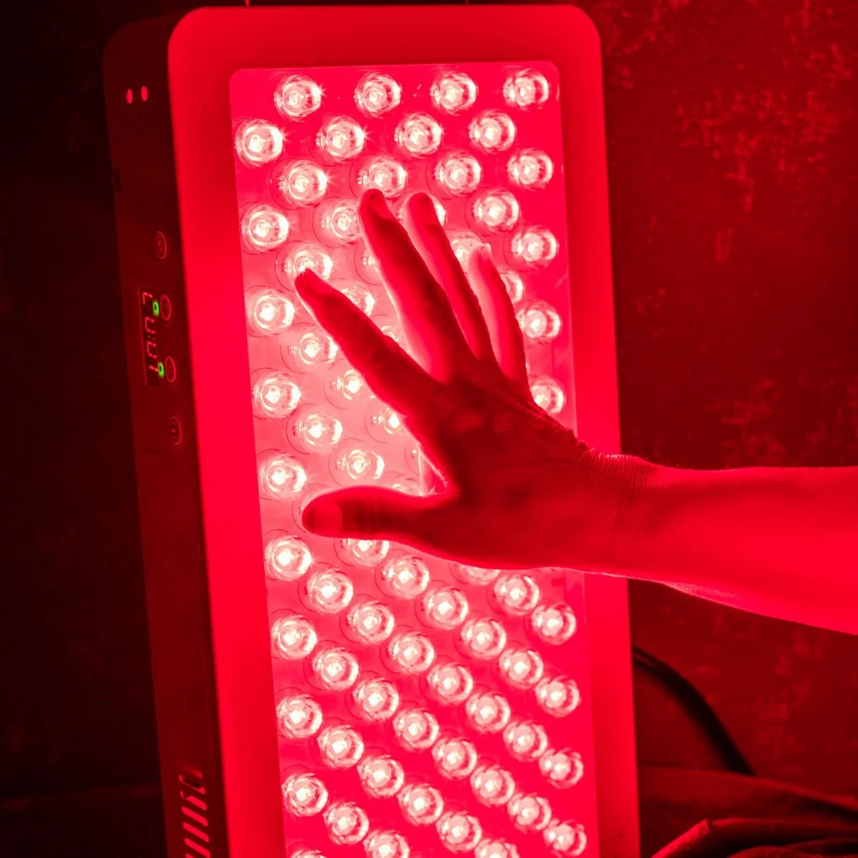 A hand is reaching out towards a red LED therapy light panel.