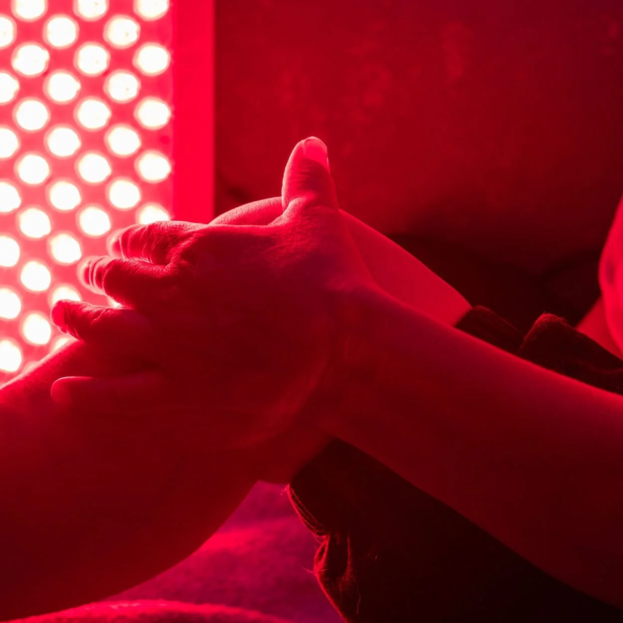 A person lying on their back in a dark room illuminated by red light, with their head tilted back and eyes closed, wearing a black collar around their neck.