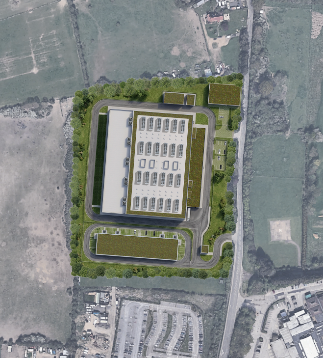 Aerial view of a data centre building with solar panels on the roof, surrounded by parking, roadways, greenery, and nearby fields.