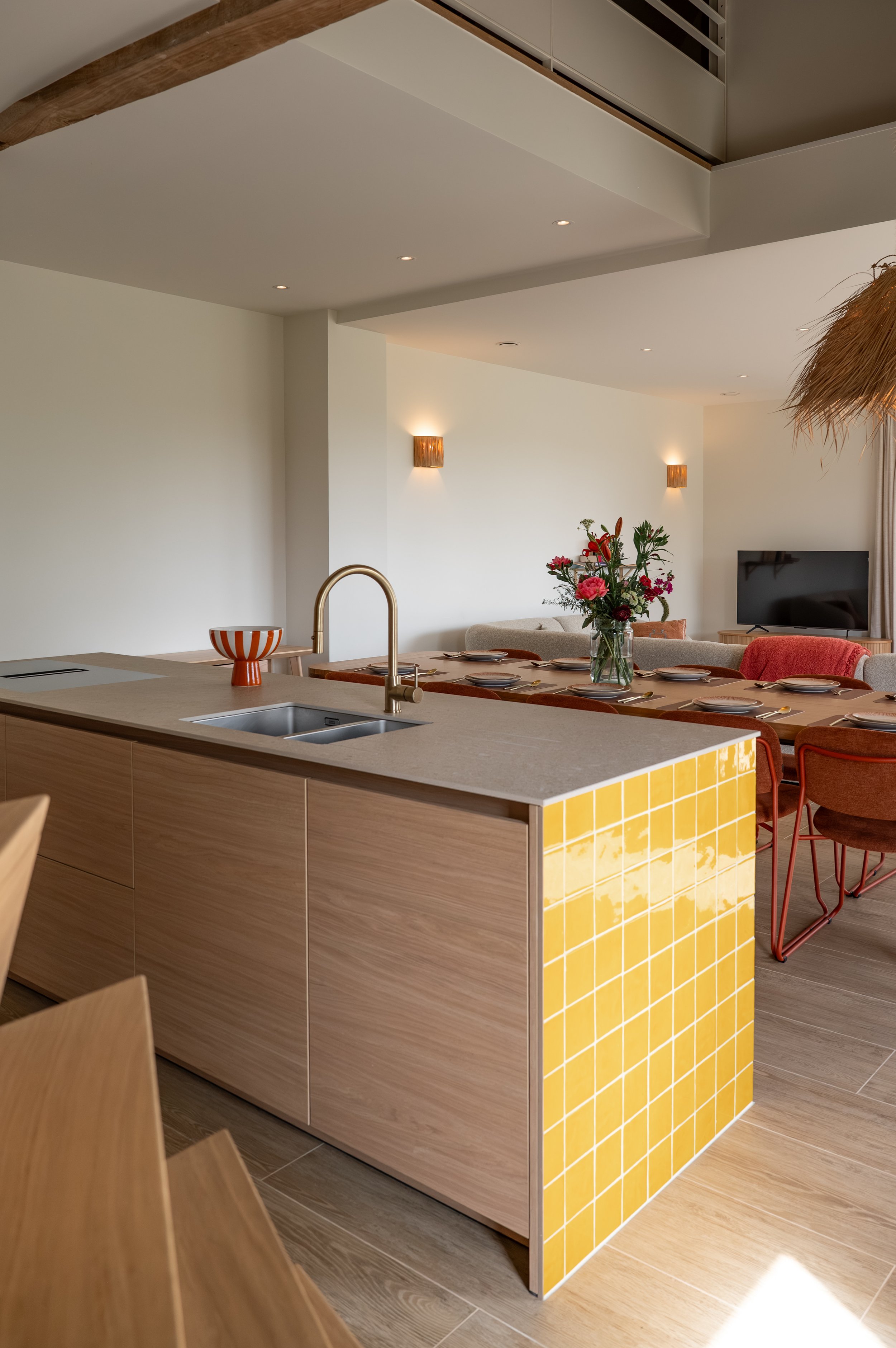 Contemporary living room with a kitchen island, a vase of flowers, a wall-mounted TV, and modern lighting.