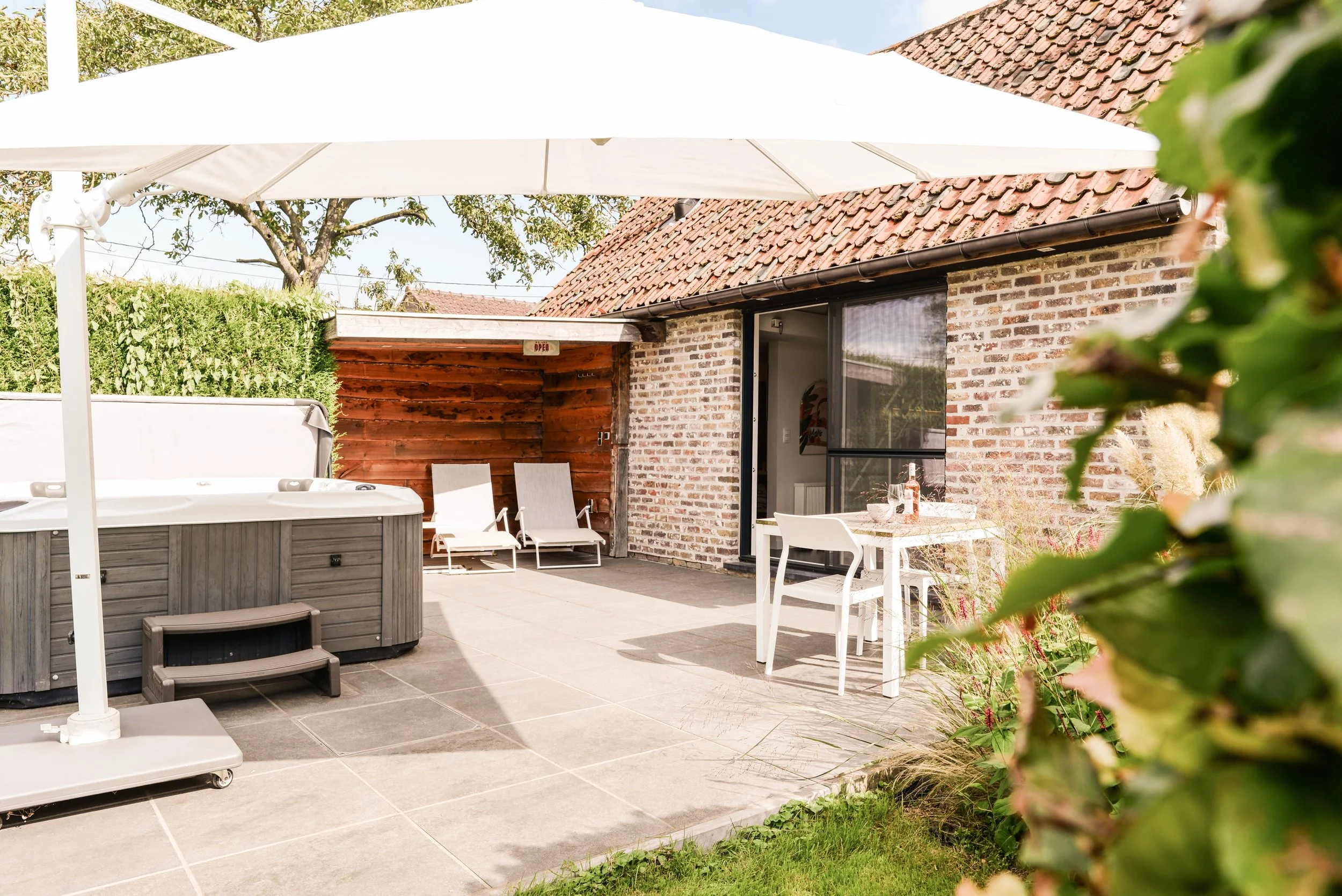 Private sunny terrace with jacuzzi and sunbeds, overlooking the fruit garden at WellNest studio, next to Barn of Bliss corporate offsite venue near Bruges.