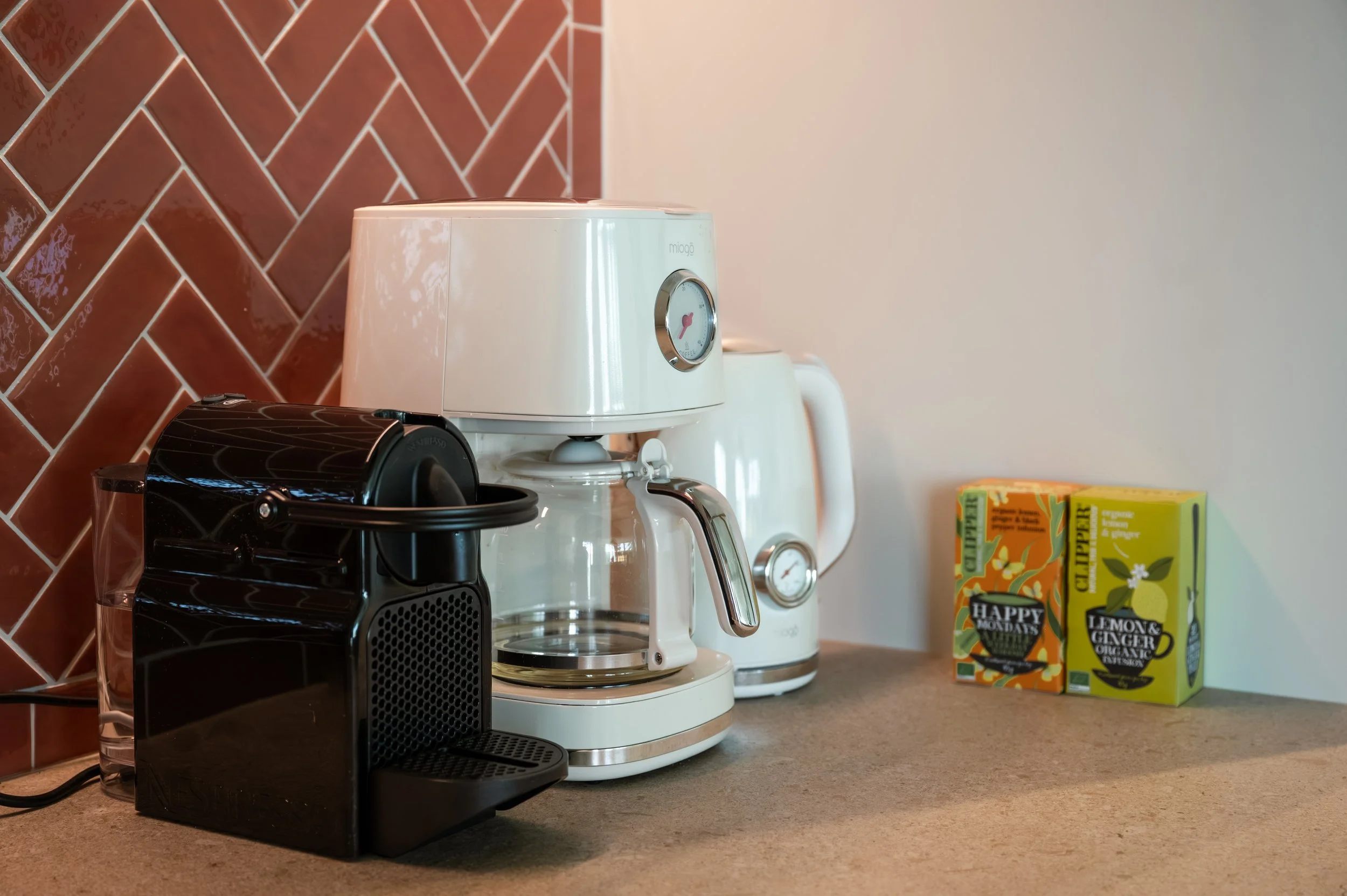Coffee maker and espresso machine on kitchen counter with boxes of tea on the counter.
