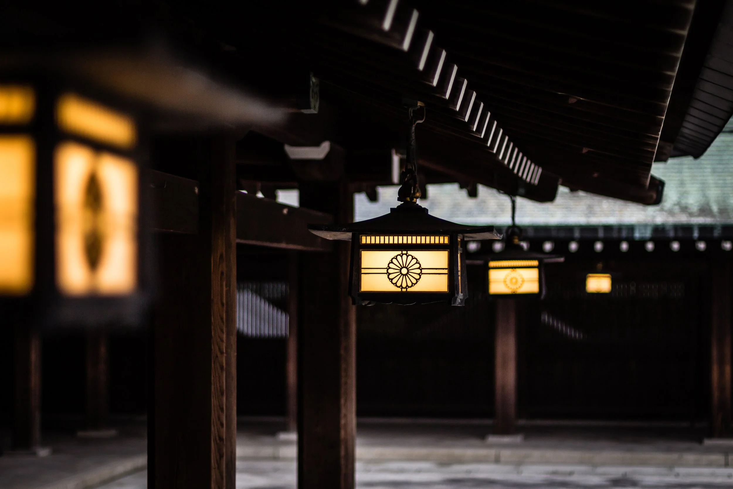 Traditional Japanese lanterns hanging under a wooden roof eave at dusk, with dimly lit background.