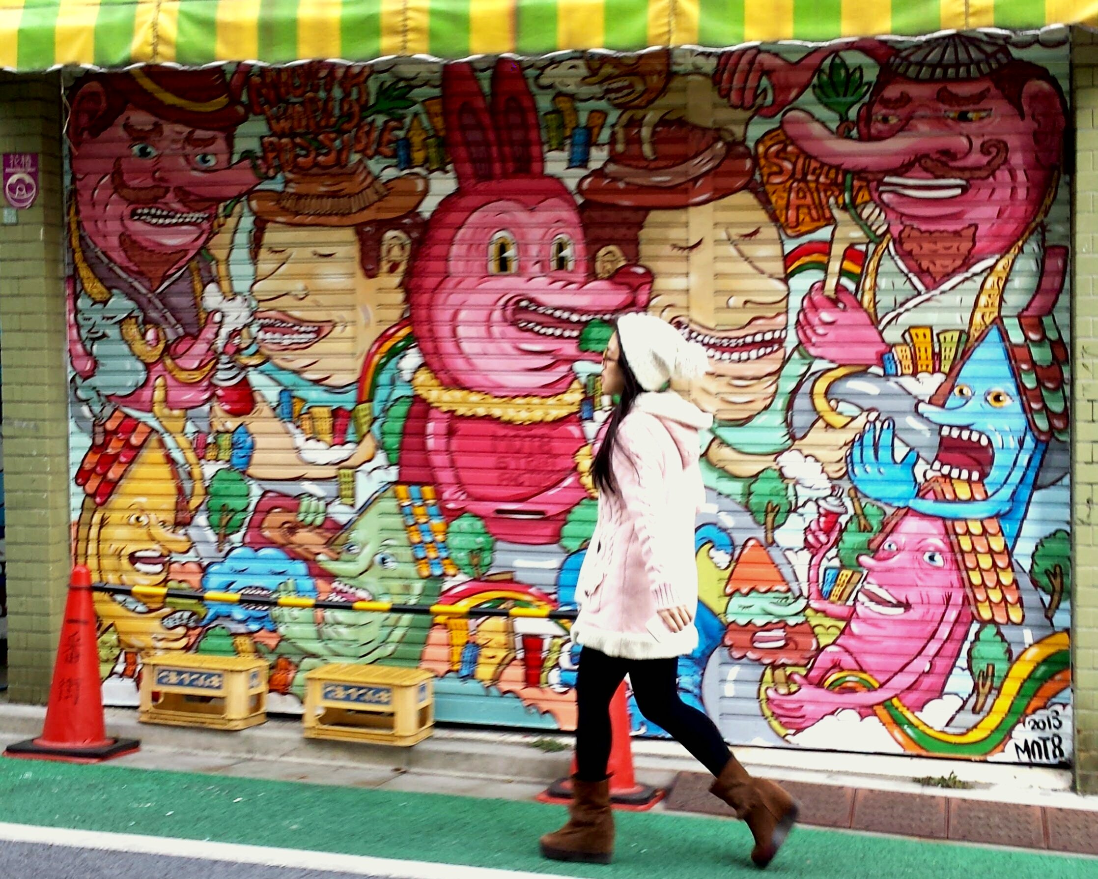 A woman walking past a colorful mural featuring cartoon-like mythical creatures and characters on a city street.