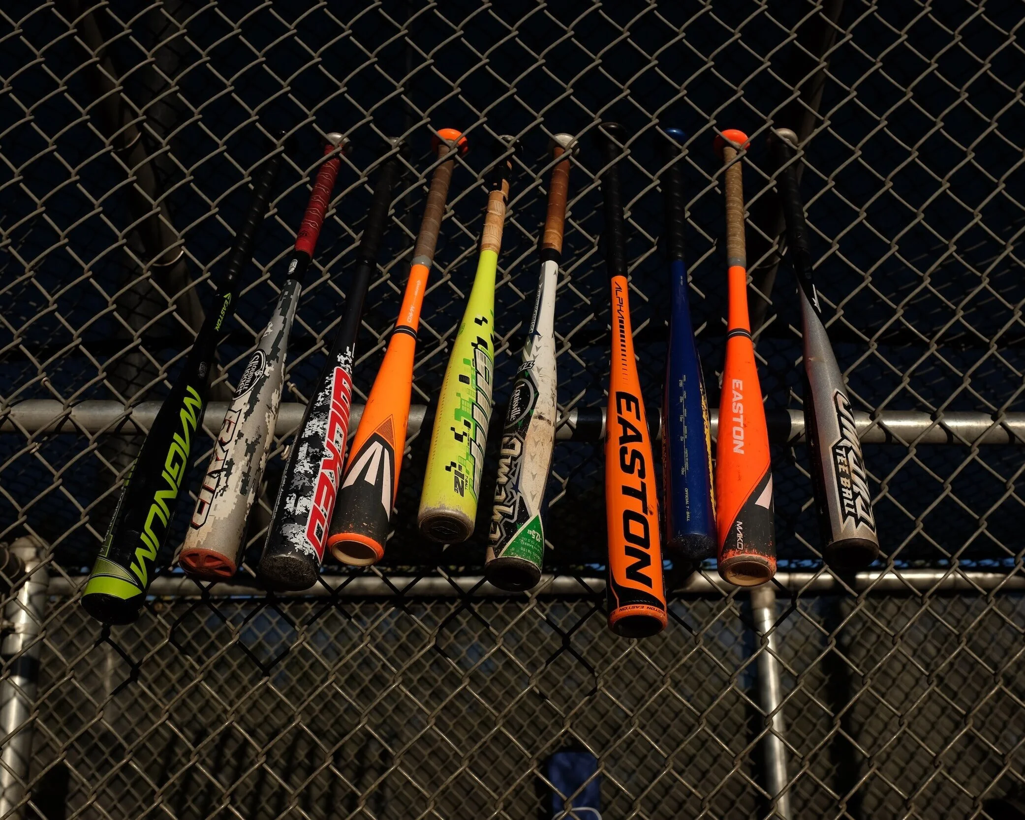 Twelve tennis rackets hanging on a chain-link fence at a tennis court.
