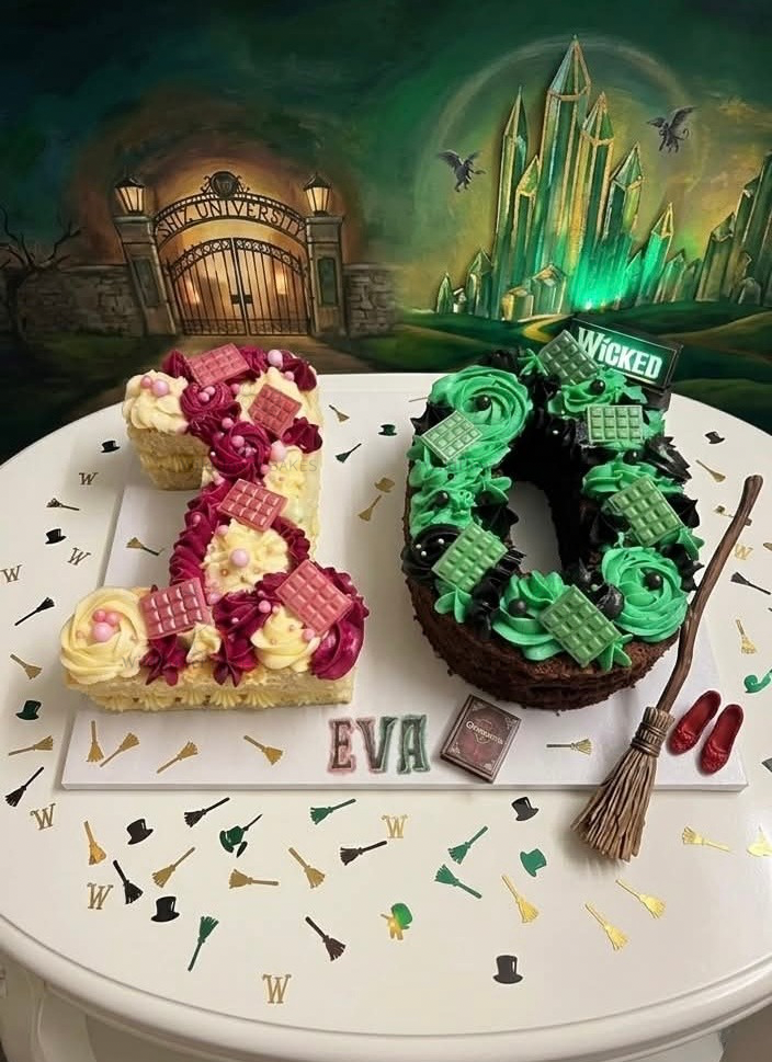 Number cake decorated with Wicked theme, featuring a pink and white vanilla cake in a number 1 shape, and a chocolate cake shaped as a 0 with green and black Witch-themed decorations, including a broomstick, on a white table with themed toppers.