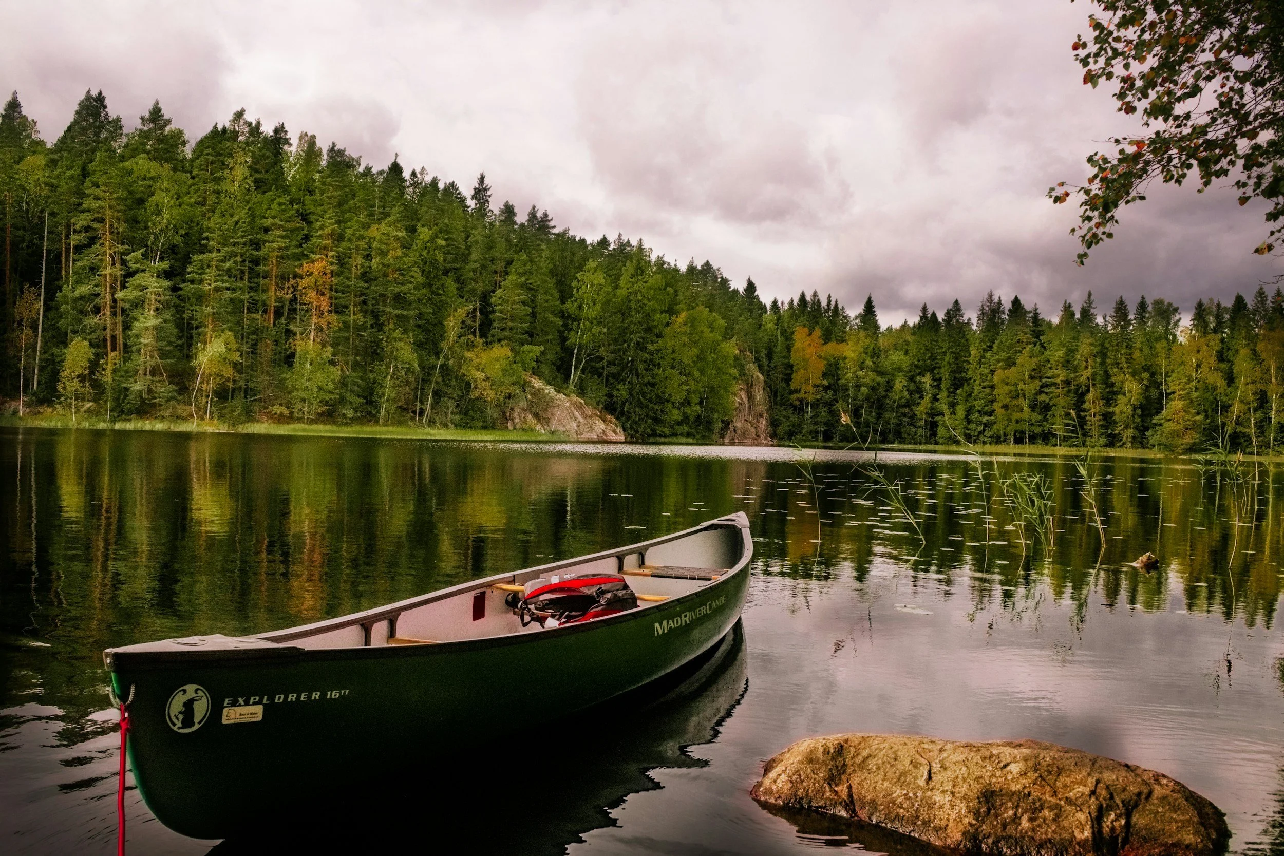 Finland, a landscape view of a canoe floating on a calm lake surrounded by dense green trees with a cloudy sky overhead.