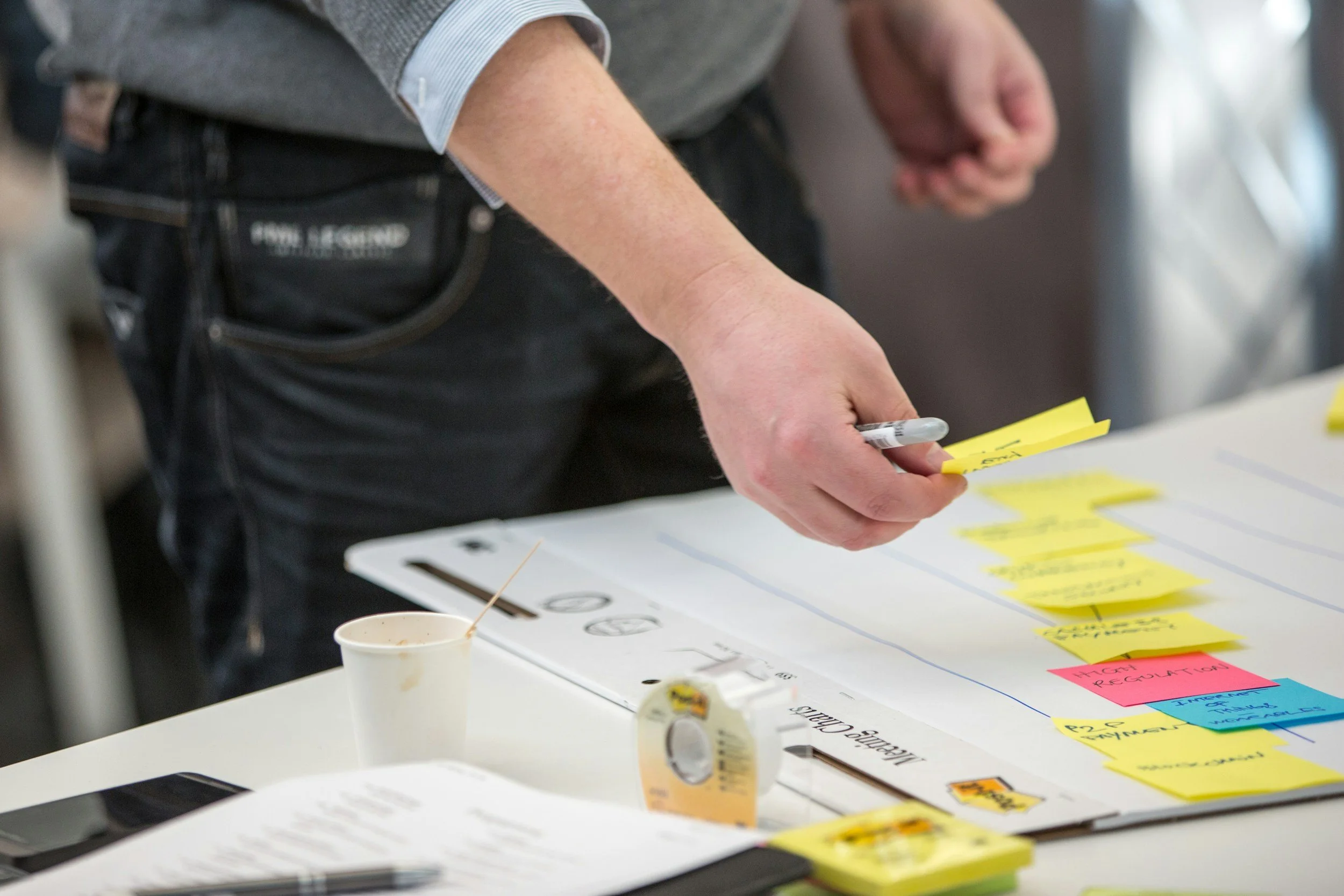 Person in a gray shirt writing on sticky notes on a table with notes and markers.