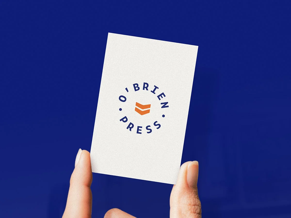 Person holding a white card with a logo and the words 'O'Brien Press' printed on it, against a blue background.