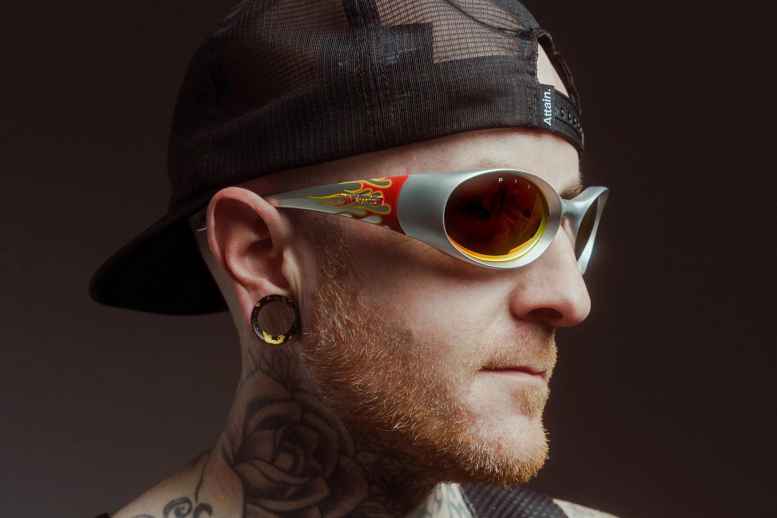 Close-up of a male athlete wearing a black cap and Pit Viper sunglasses with flames and the word 'blazer' on the side, looking to the right 