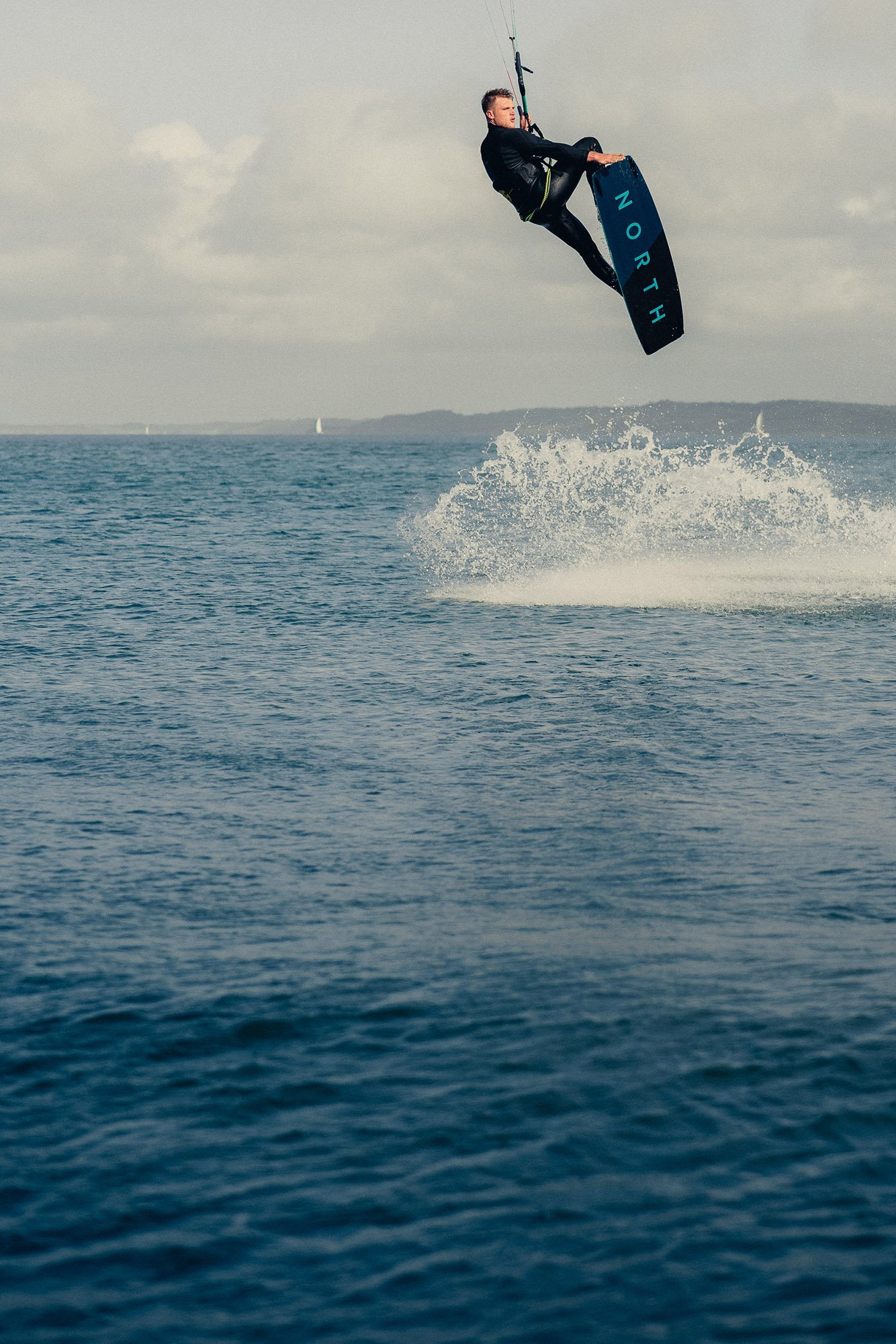 Kitesurfer doing tricks on a kiteboard in the air during daytime, with water splashing. 