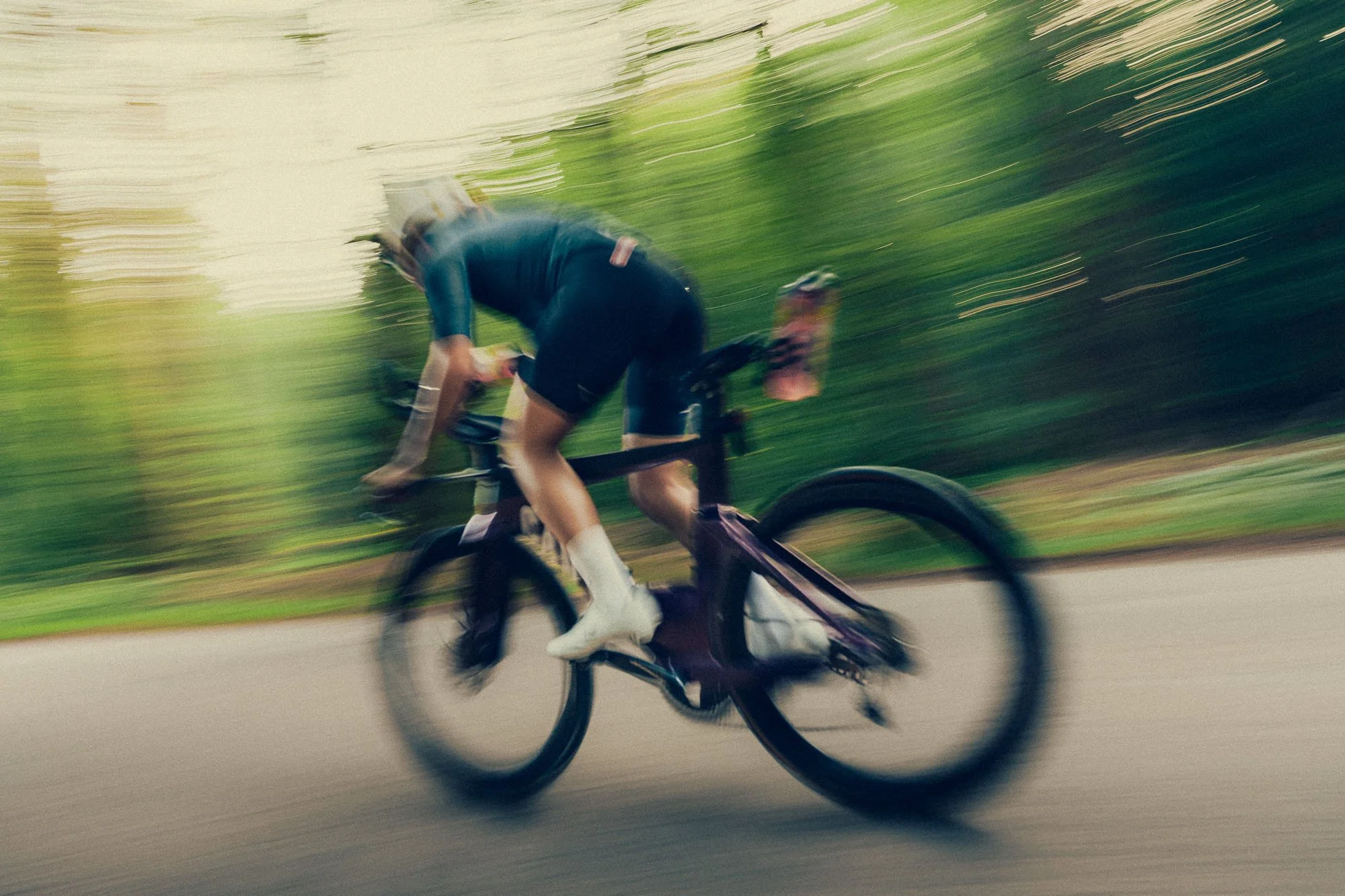 A cyclist riding a road bike on a road with blurred green trees in the background.