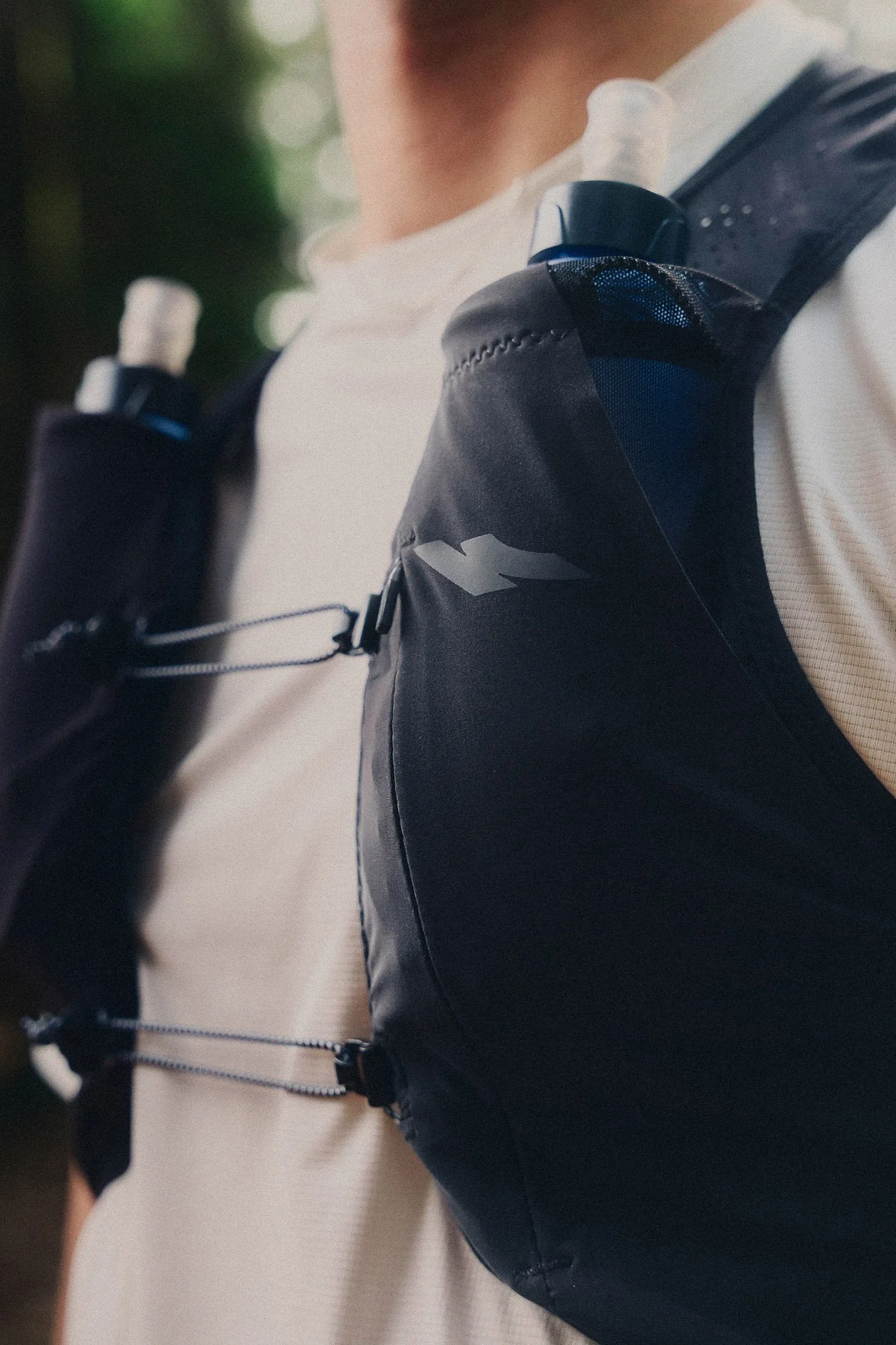 Close-up of a person wearing a Kiprun running vest with soft flasks in the pockets, outdoors with a blurred green background.