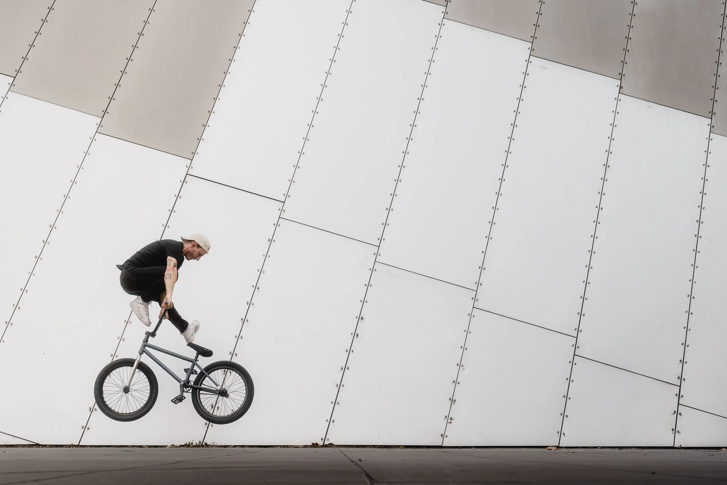 A man riding a BMX bike against a modern, metallic wall with a diagonal pattern of panels.