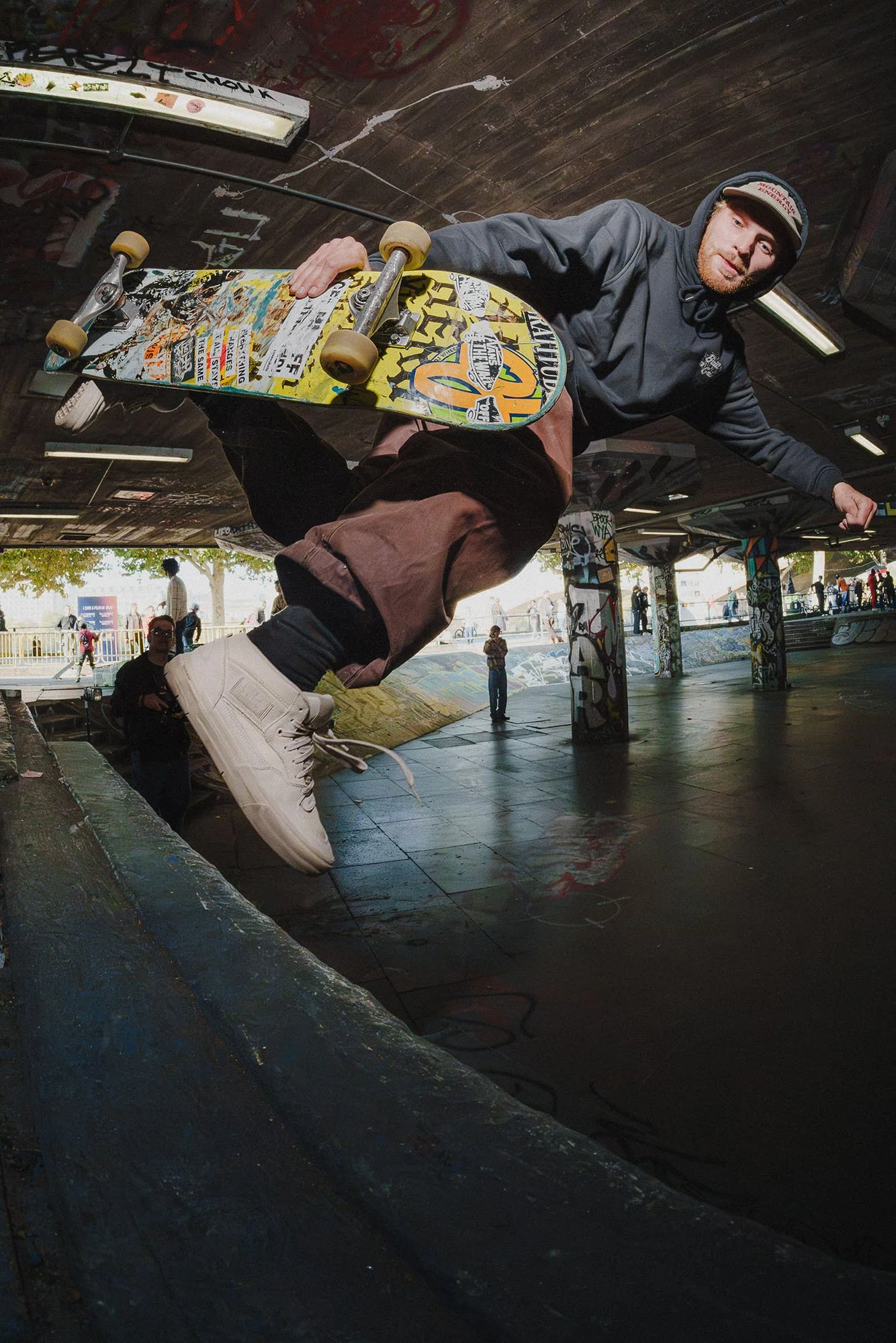 A skateboarder in a hoodie and brown pants performing a trick on a skateboard in South Bank 