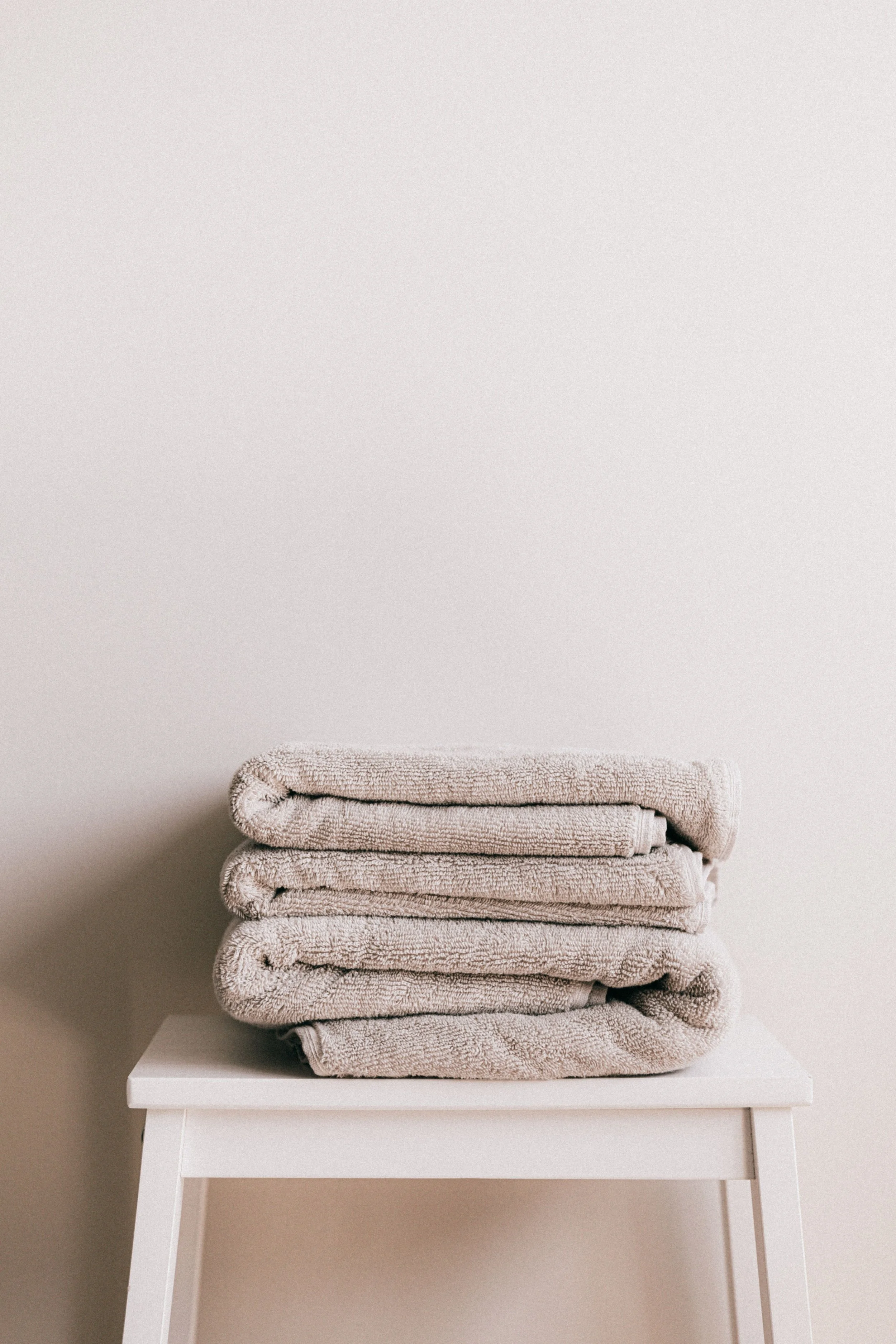 Stack of beige towels folded on a white table against a plain light-colored wall.