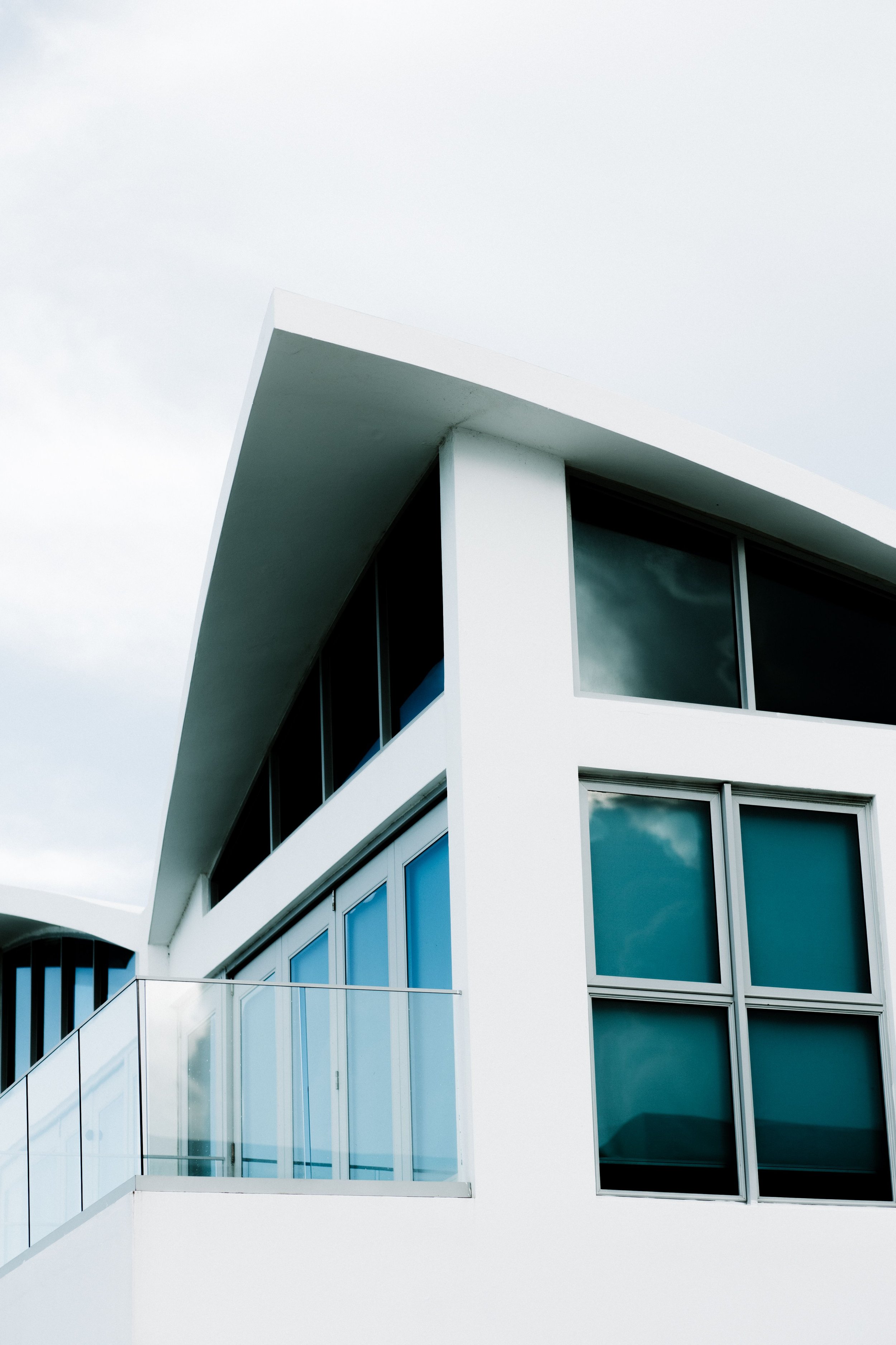 Modern white building with large reflective glass windows on a cloudy sky day.