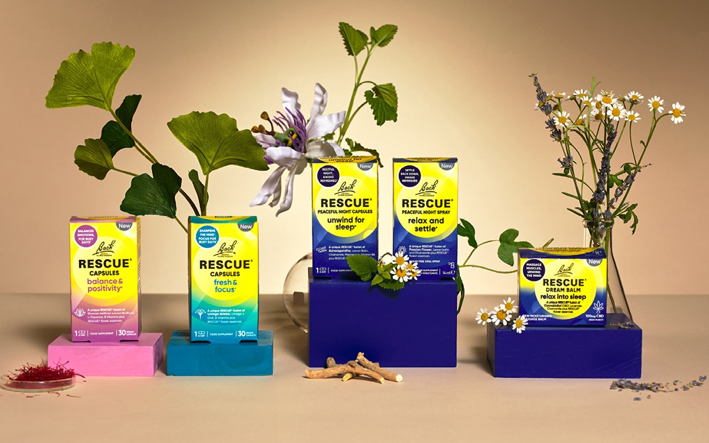 An arrangement of Rescue brand sleep aid products with plants and flowers. From left to right: pink and purple box, yellow and blue box, purple box with tall plant, yellow and black box, yellow and blue box, blue box with white and yellow box on top, yellow and blue box with daisies and lavender in vases.