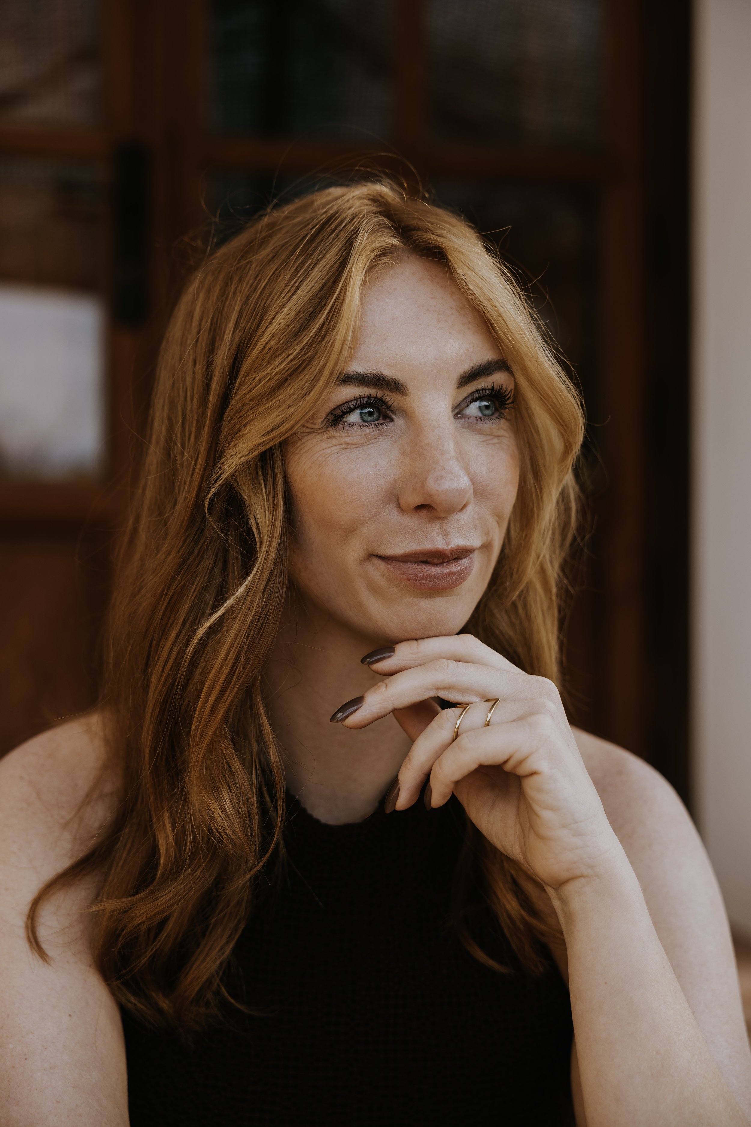 Madelon Roodnat, eigenaresse LONN. Close-up van een vrouw met rood haar, blauwe ogen, en een glimlach, zittend met haar hand onder haar kin.