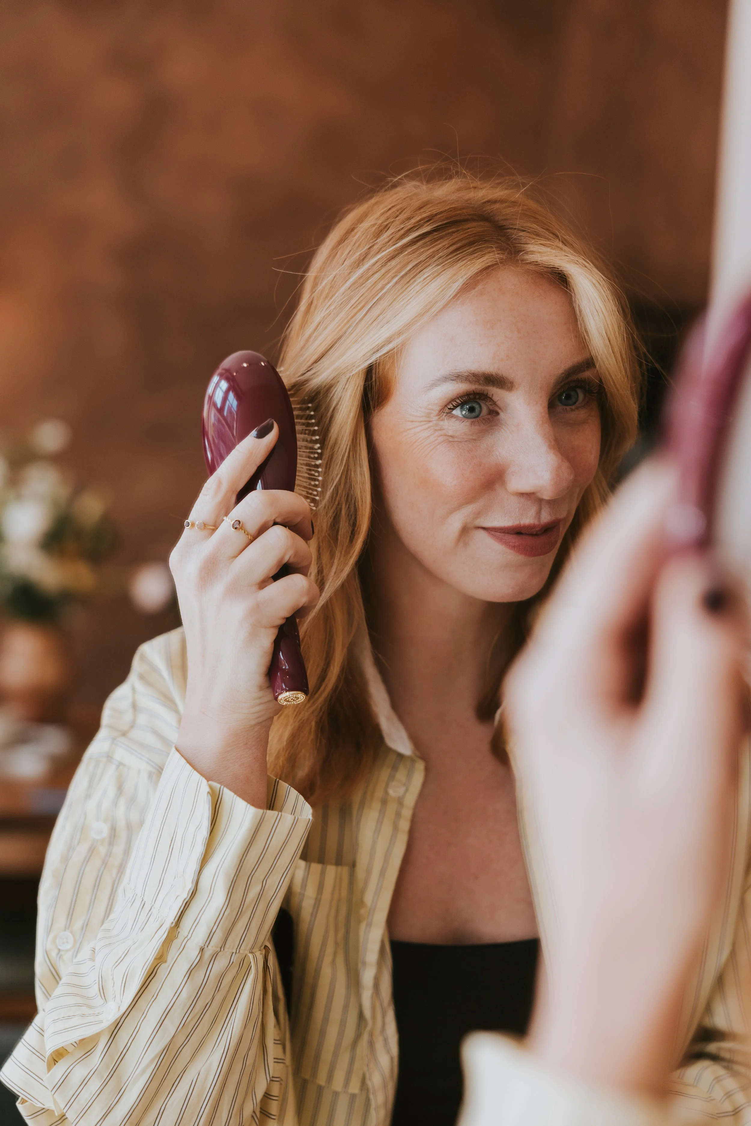 Eigenaresse salon Madelon Roodnat, vrouw kamt haar roodharige haar terwijl ze naar zichzelf in de spiegel kijkt. Hoge kwaliteit producten haarborstel van merk La Bonne Brosse. Te koop ook in de salon