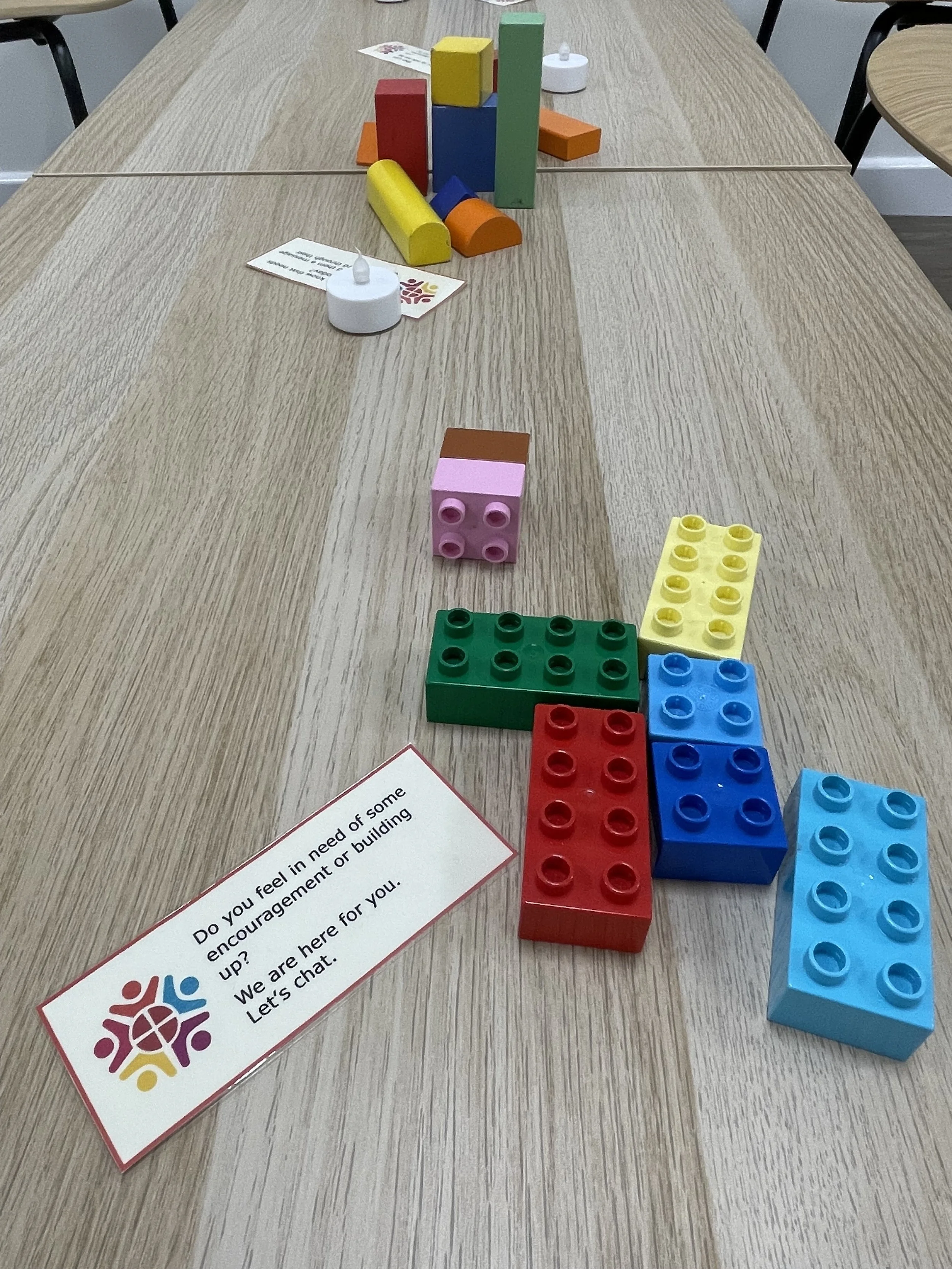 Colorful building blocks arranged on a wooden table with a piece of paper containing text.
