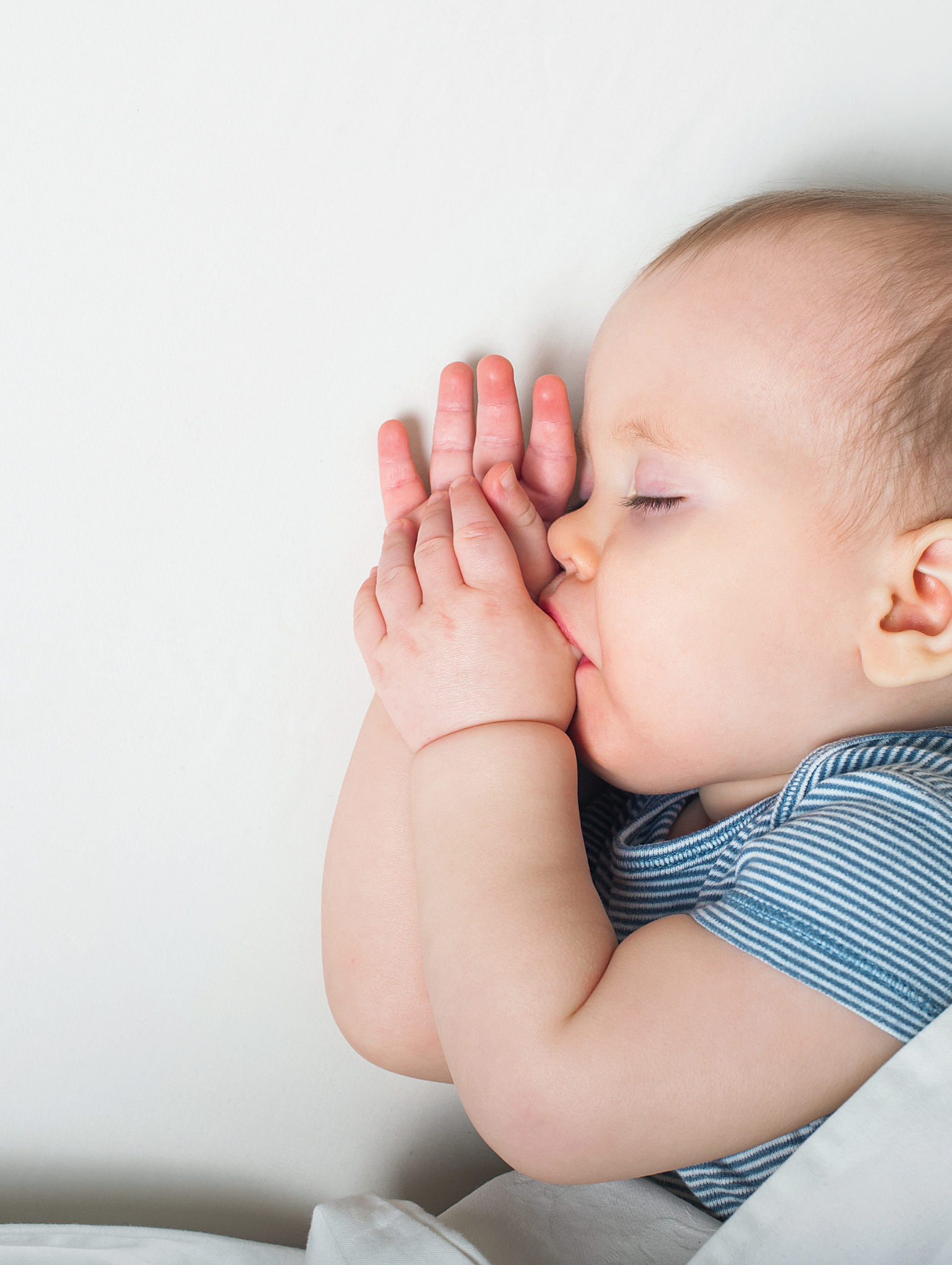 Close-up of a young child with closed eyes, pressing hands together in prayer or meditation, with a white background.