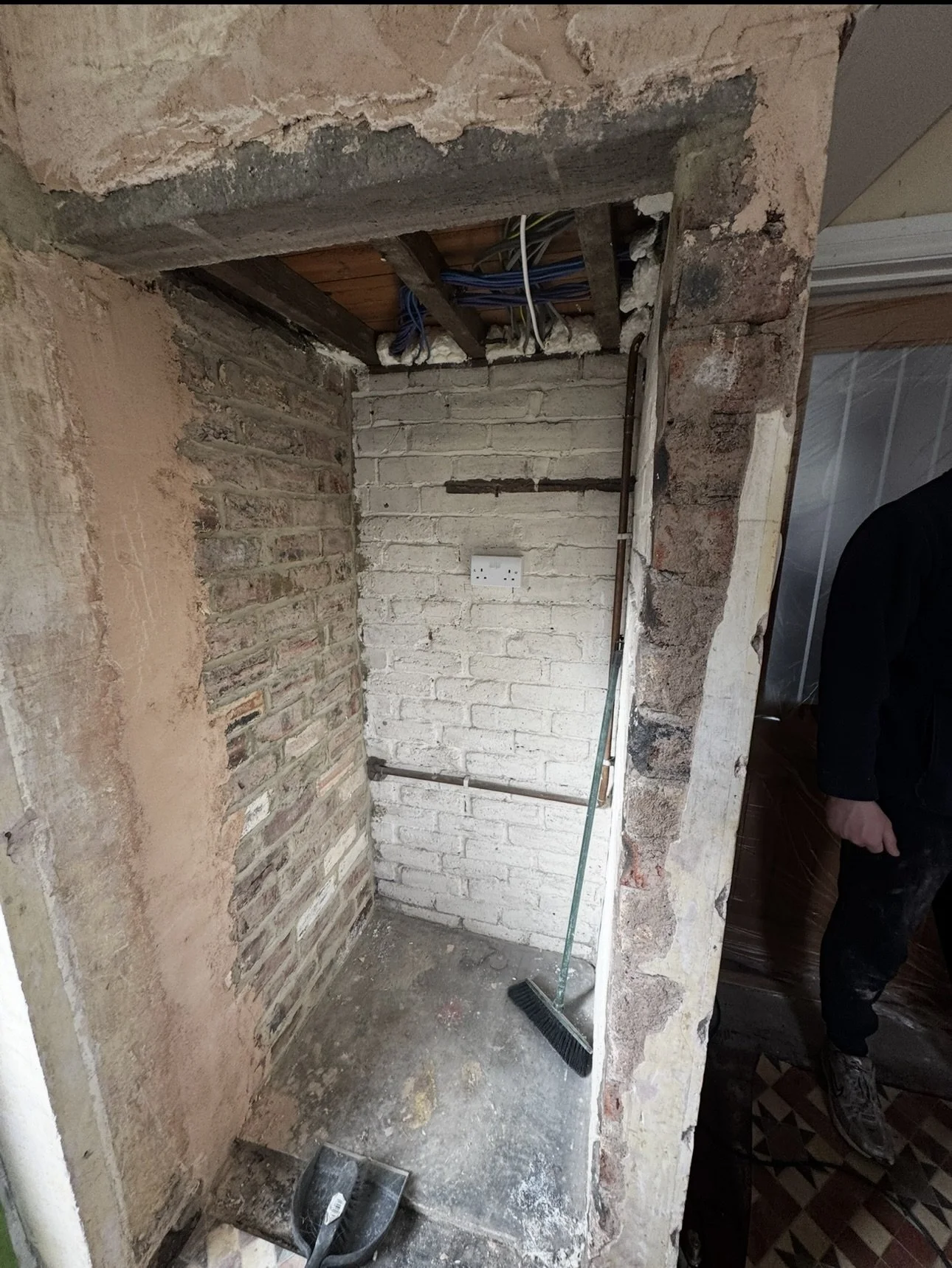 Partially demolished wall with exposed brickwork and electrical wiring, renovation tools and debris on a concrete floor.