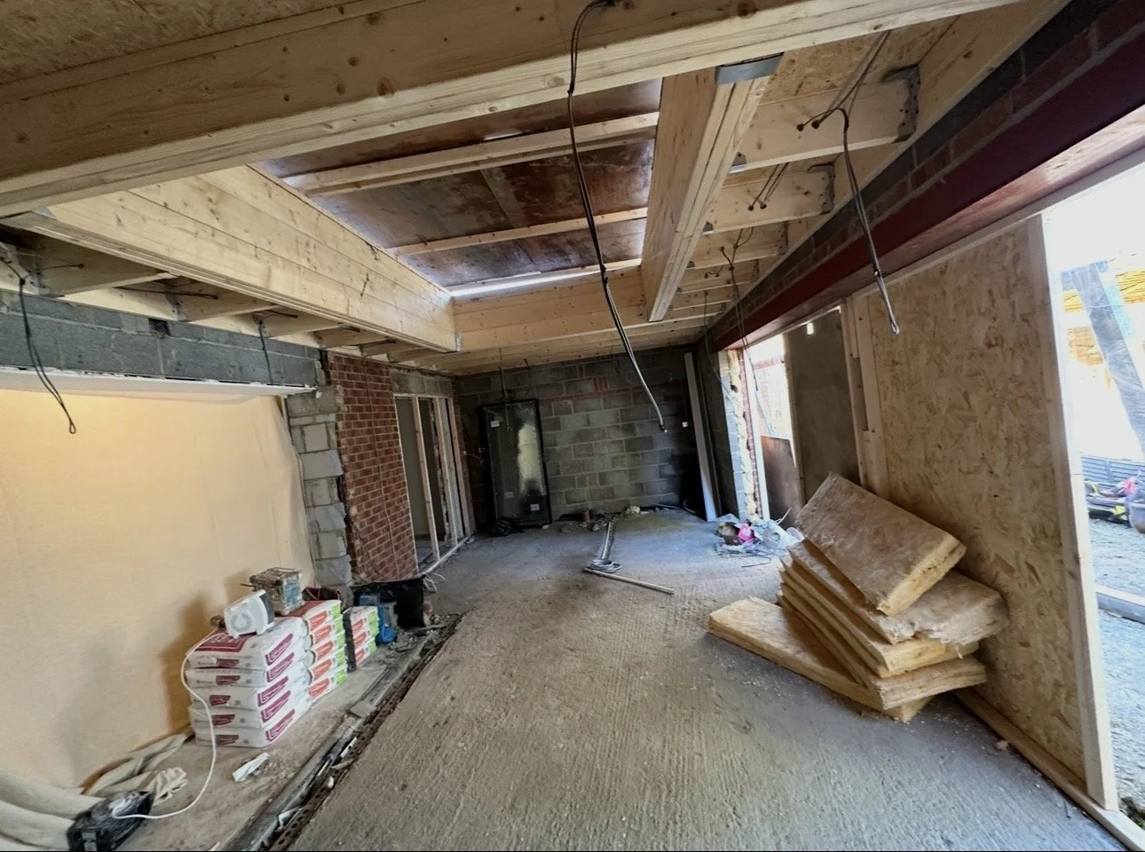 Interior of a room under construction with unfinished walls, insulation on the floor, and exposed ceiling beams.