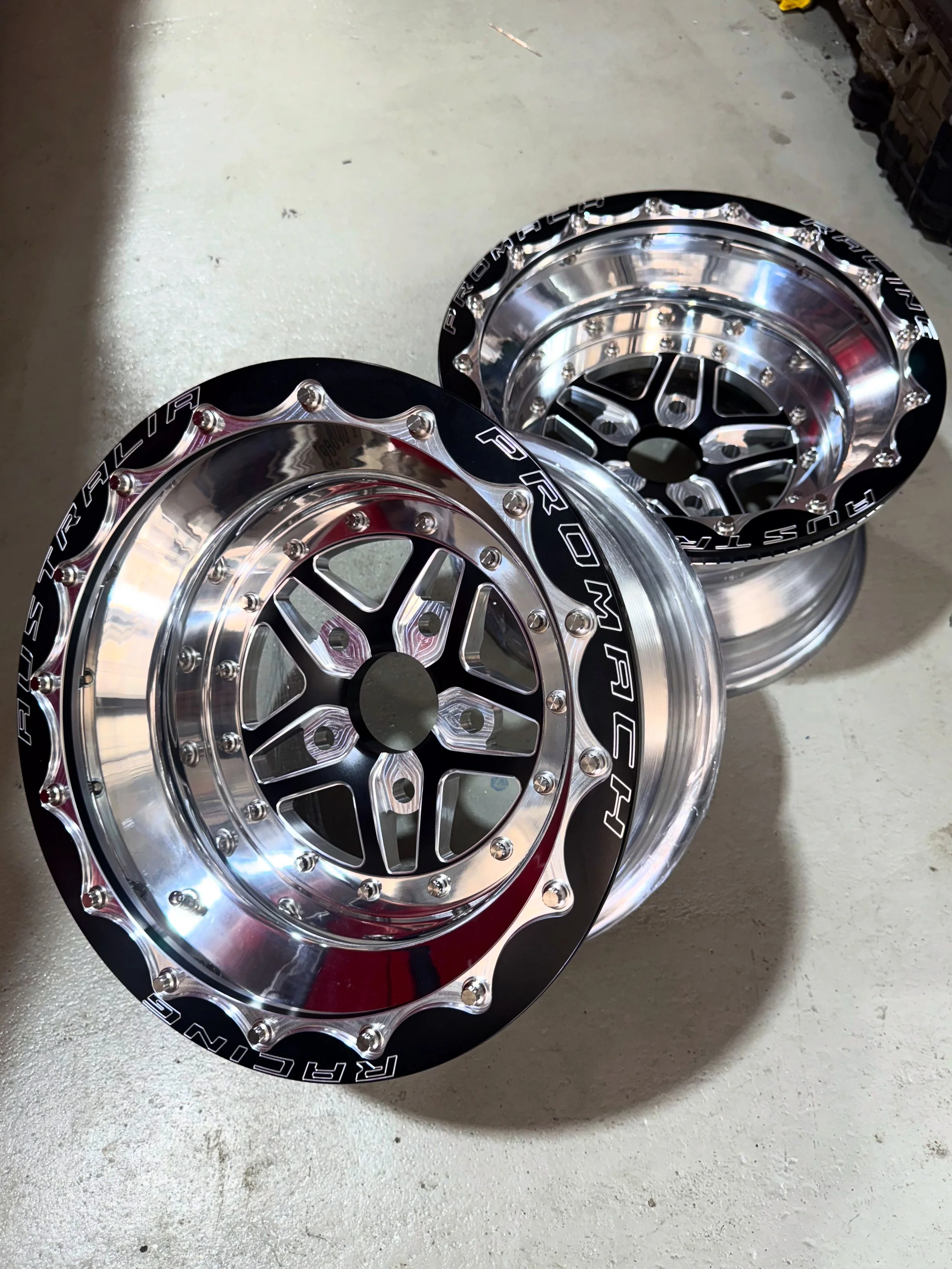 Two shiny, black and silver wheel hubs with a decorative design and the brand name "RACING RUSH" printed around the rim, resting on a concrete floor.