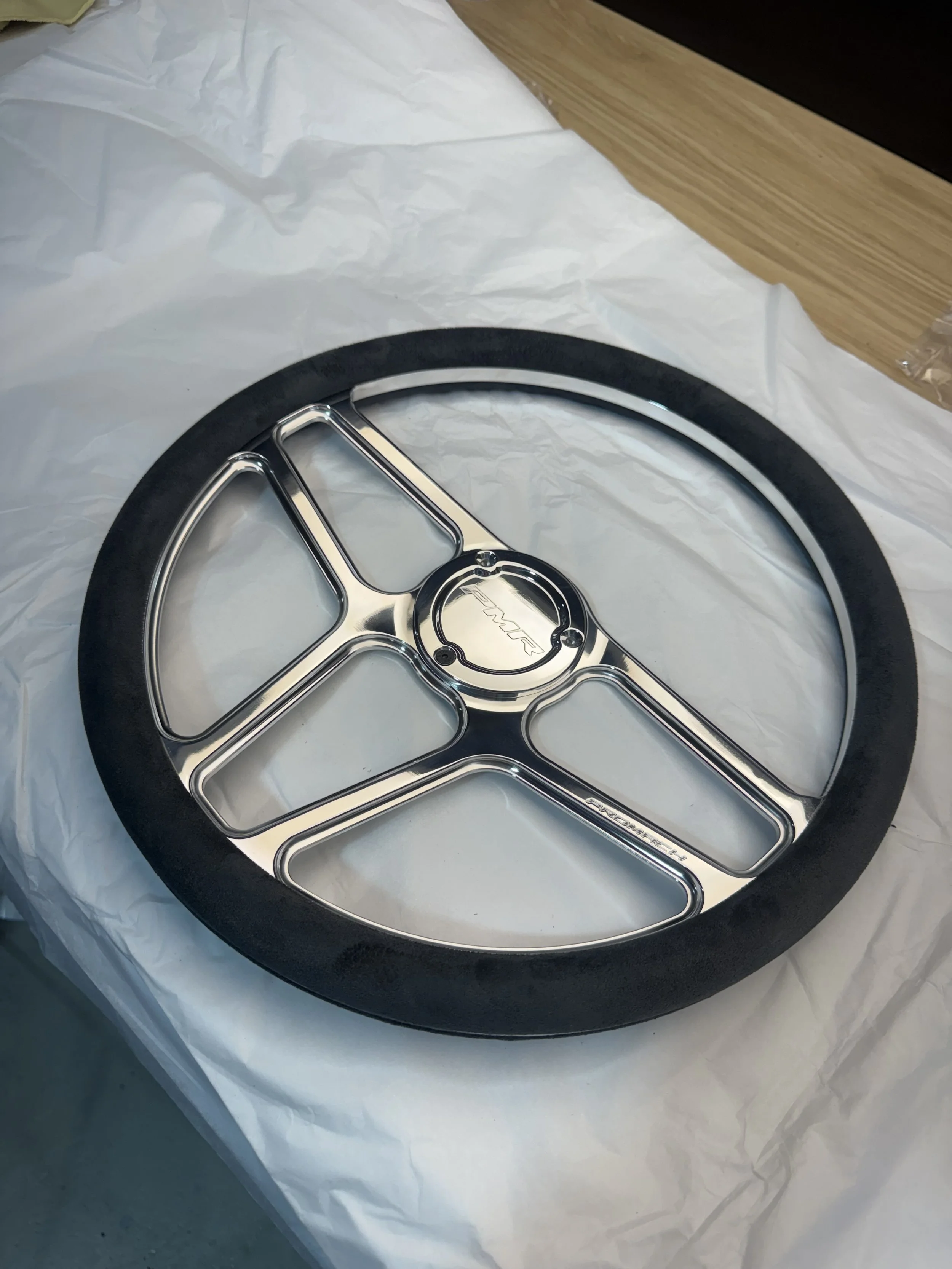 A black and silver Mercedes-Benz steering wheel cover resting on white paper on a wooden surface.
