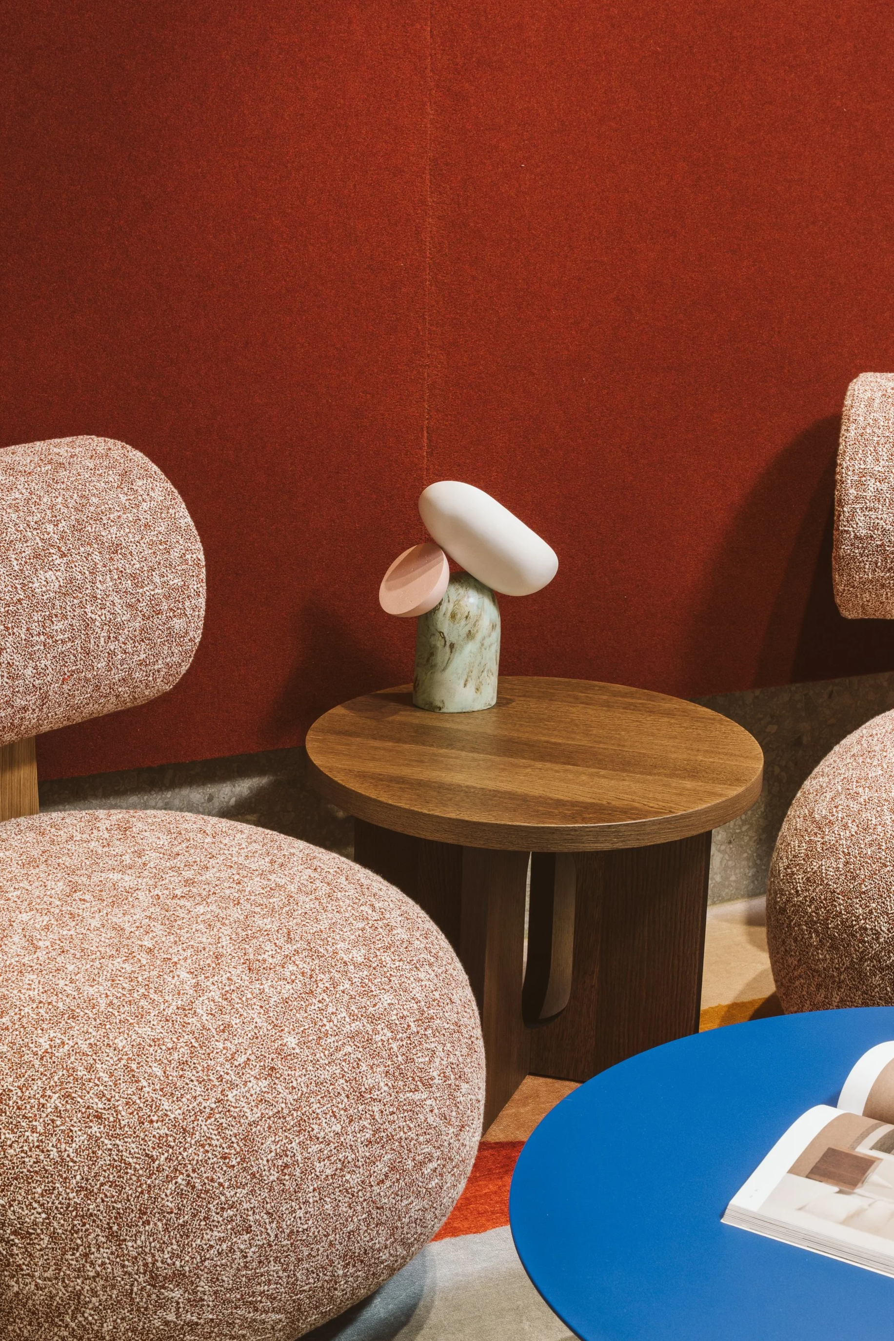 Modern interior space with pink and orange textured seating, a wooden side table with a marble sculpture, and a blue table with an open magazine on it.