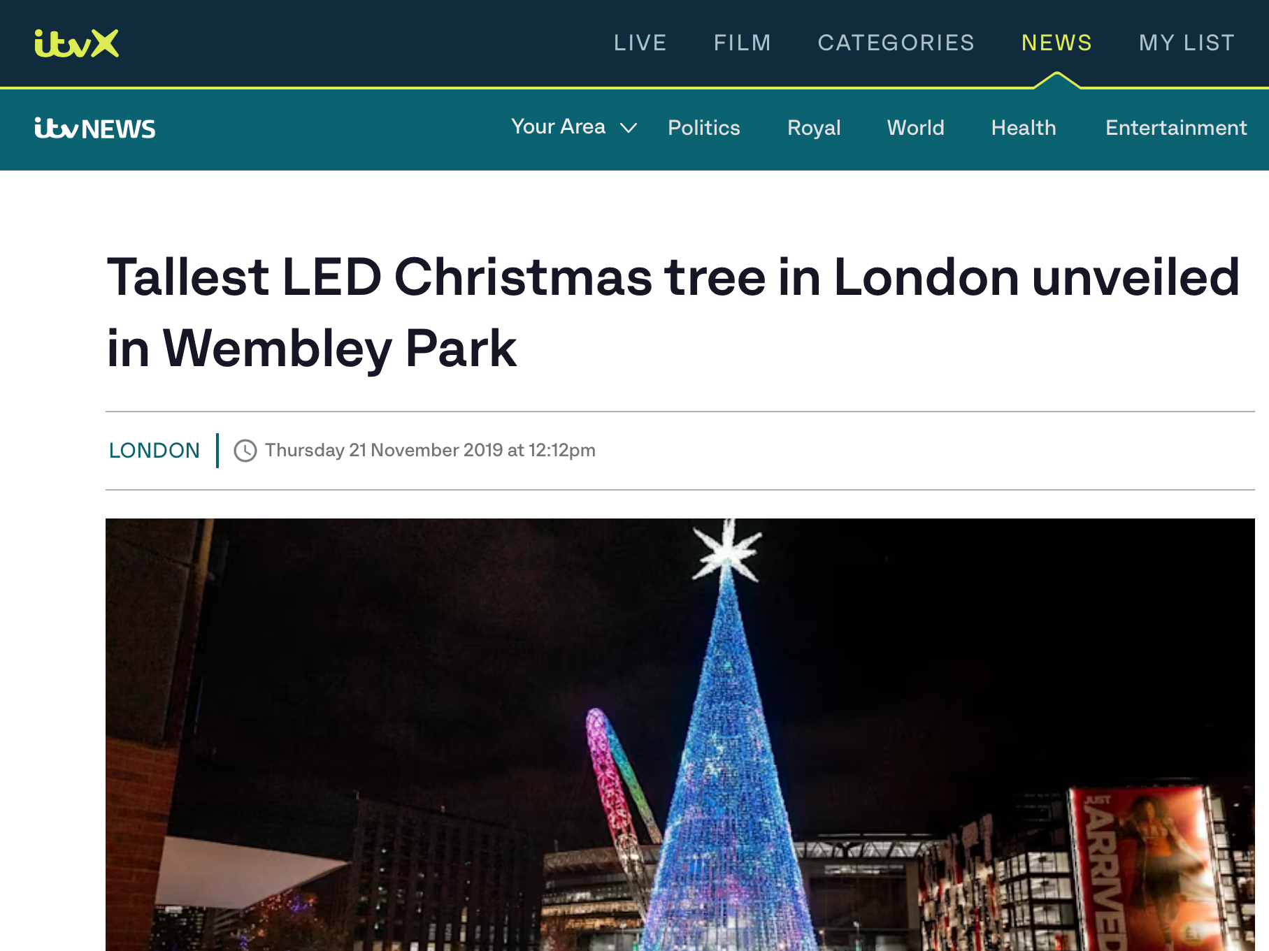 A tall, illuminated Christmas tree made of blue LED lights with a white star on top, located in Wembley Park during nighttime.