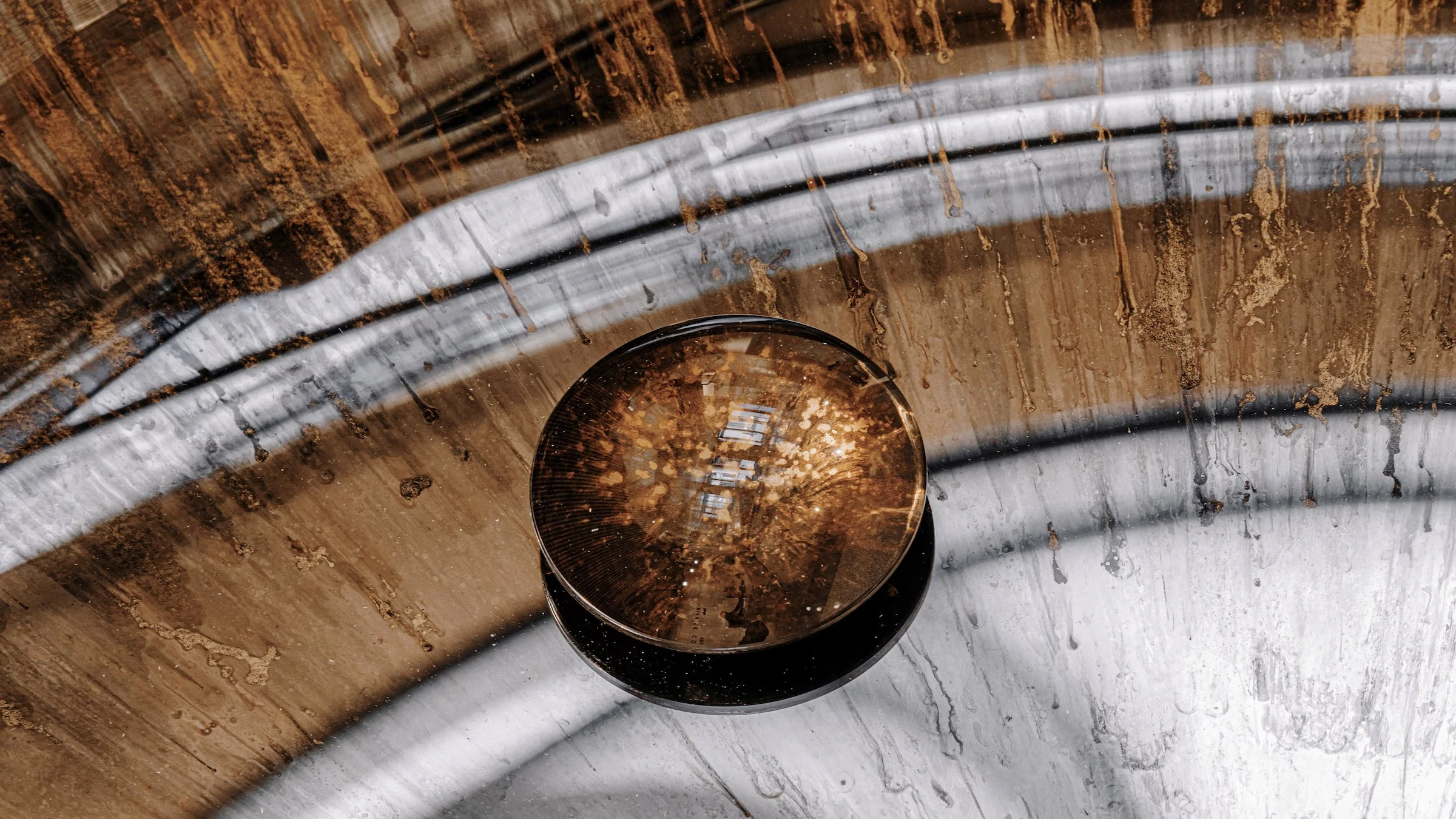 Close-up of a metallic bowl with water droplets inside on a wooden surface with water stains and a rain reflection.