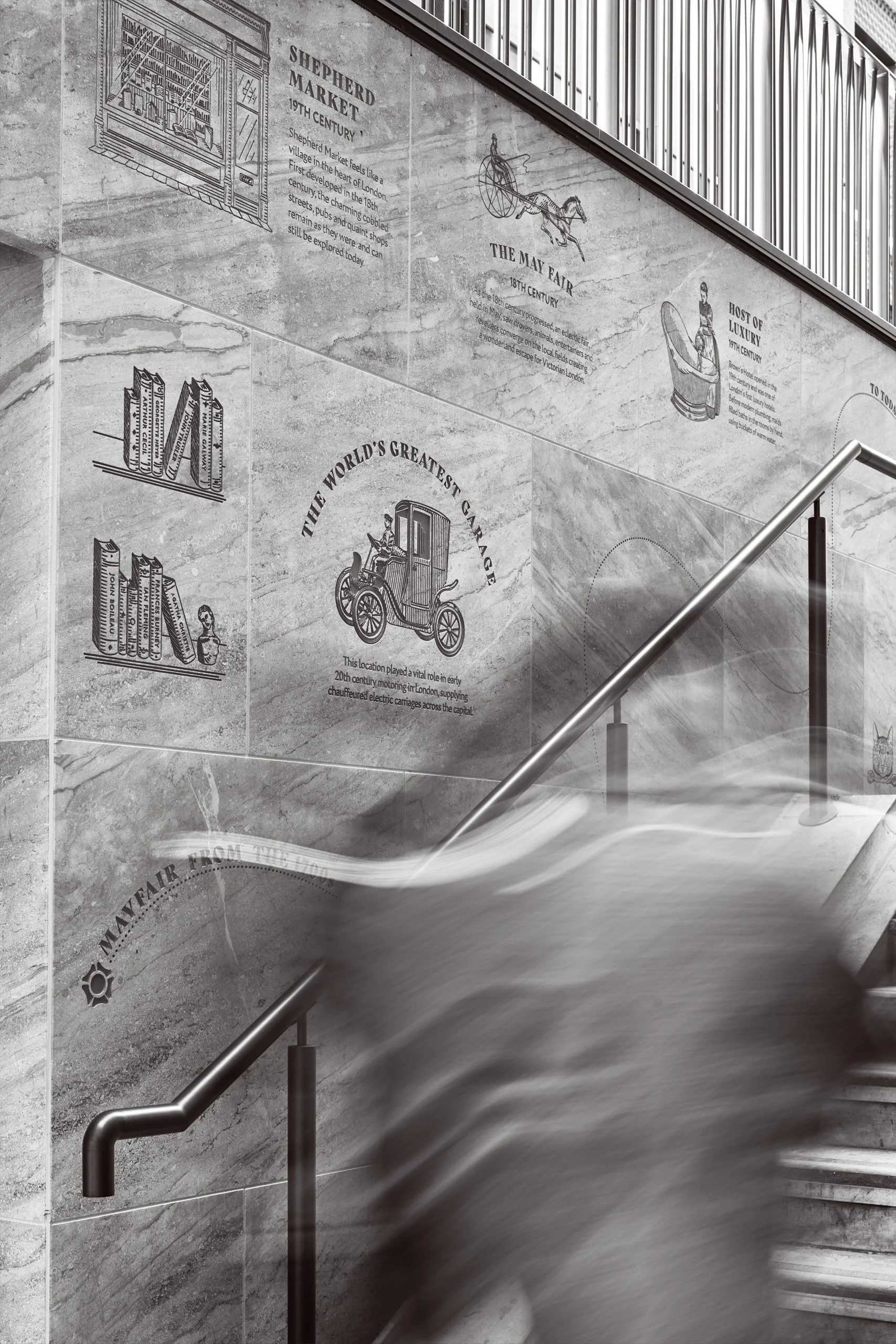 A tiled staircase with a polished metal handrail, and large monochrome mural artwork on the wall depicting historical scenes and text.