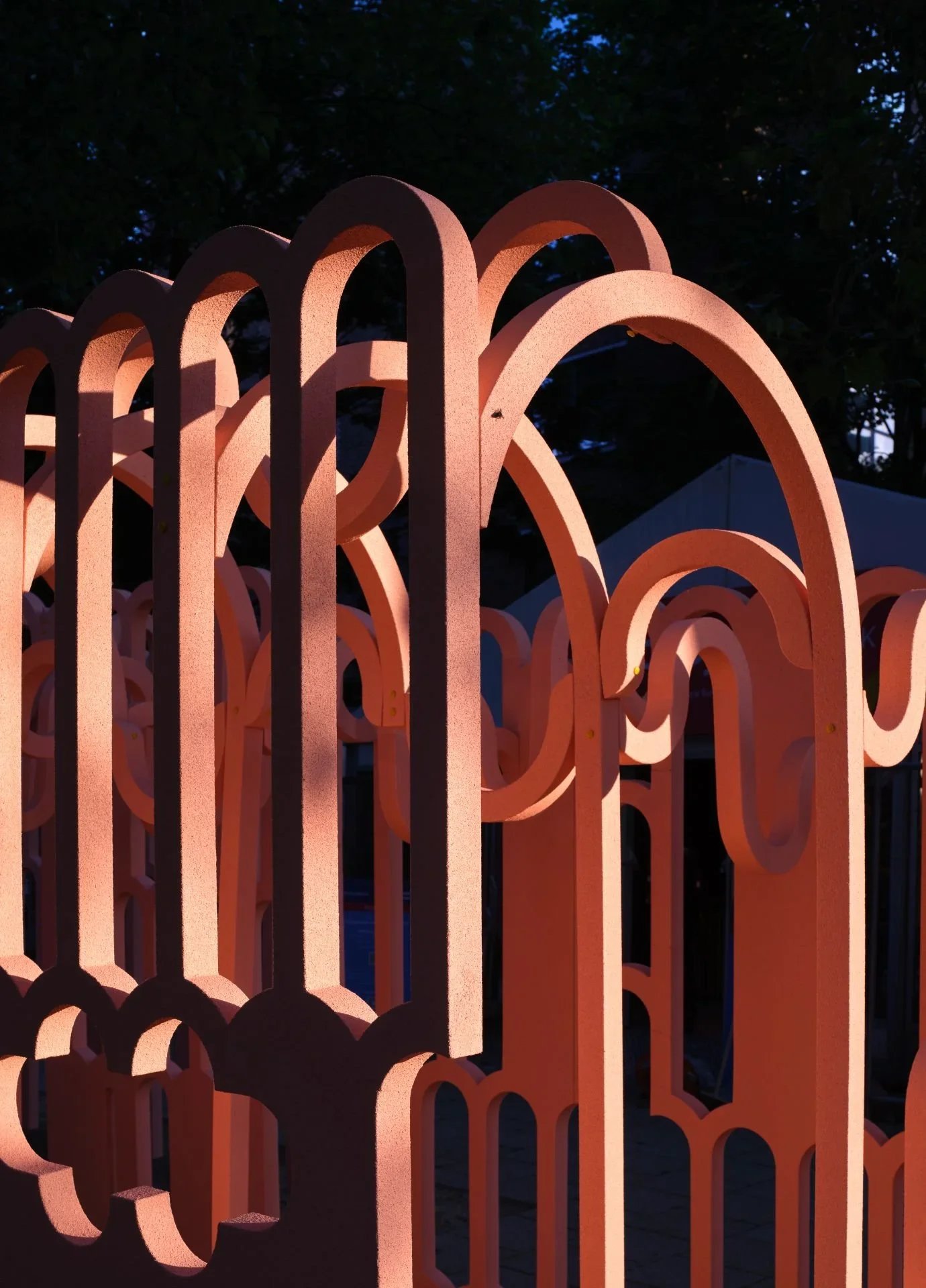 Close-up of a decorative orange metal fence with intricate patterns, taken during dusk with dark trees in the background.