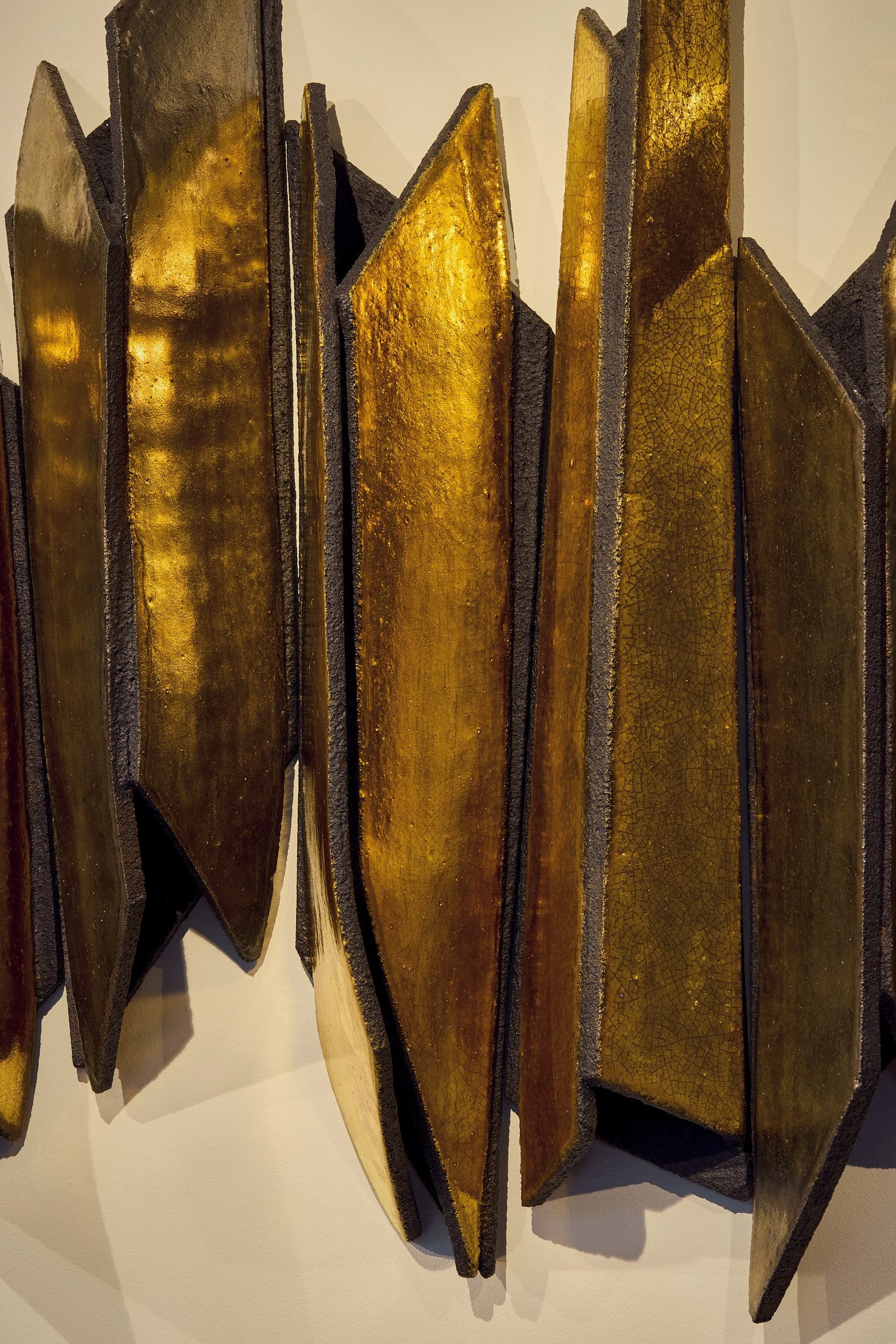 Close-up of a wall-mounted art installation made of vertically arranged rectangular panels with a golden, cracked, and textured surface, edged with dark framing.