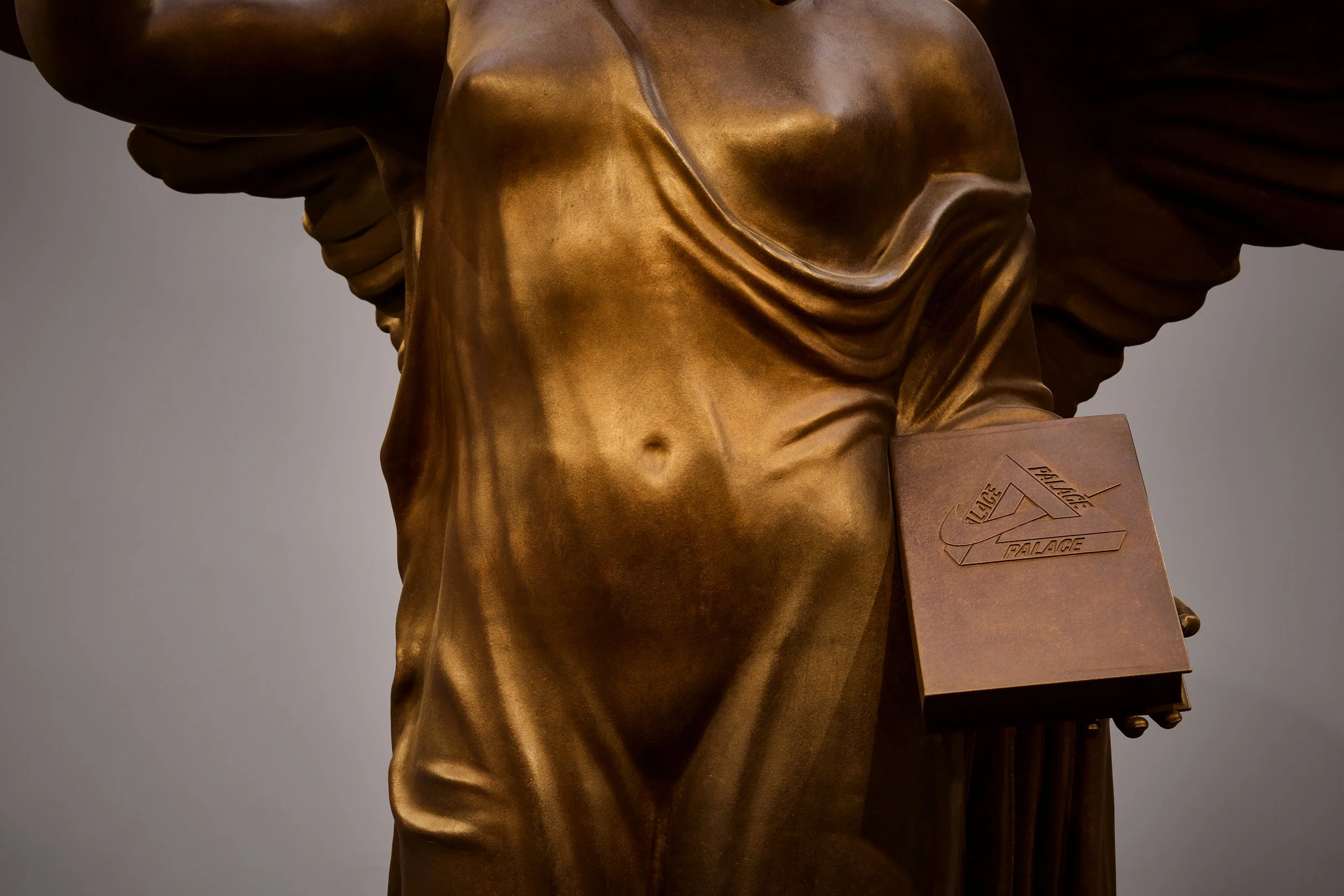 Close-up of a bronze statue of a standing man wearing a long coat, with an award plaque in his hand that displays the Palace of Fine Arts logo.