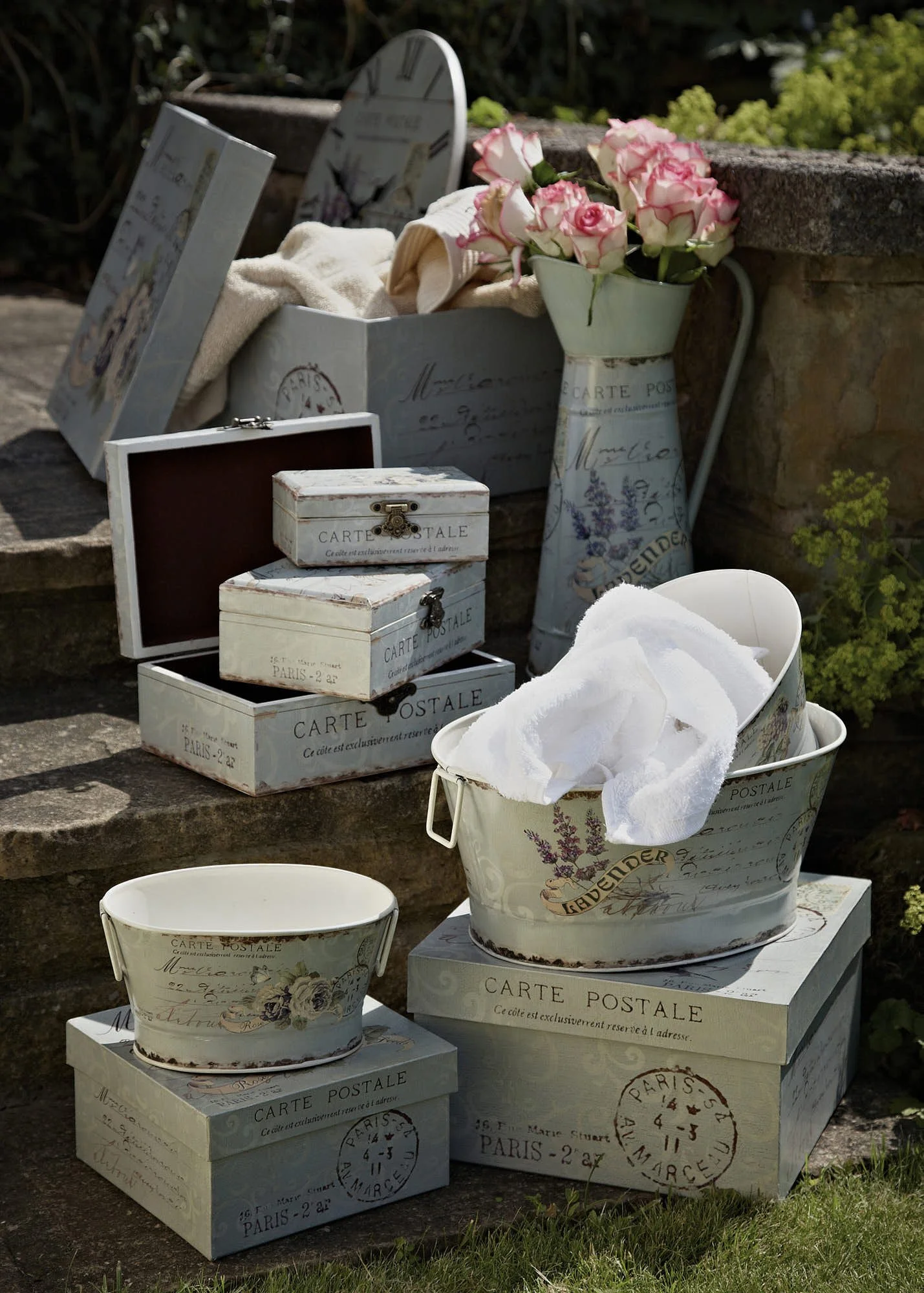 Decorative flower-themed boxes and vases with pink roses, some with white cloths, arranged outdoors on stone steps.