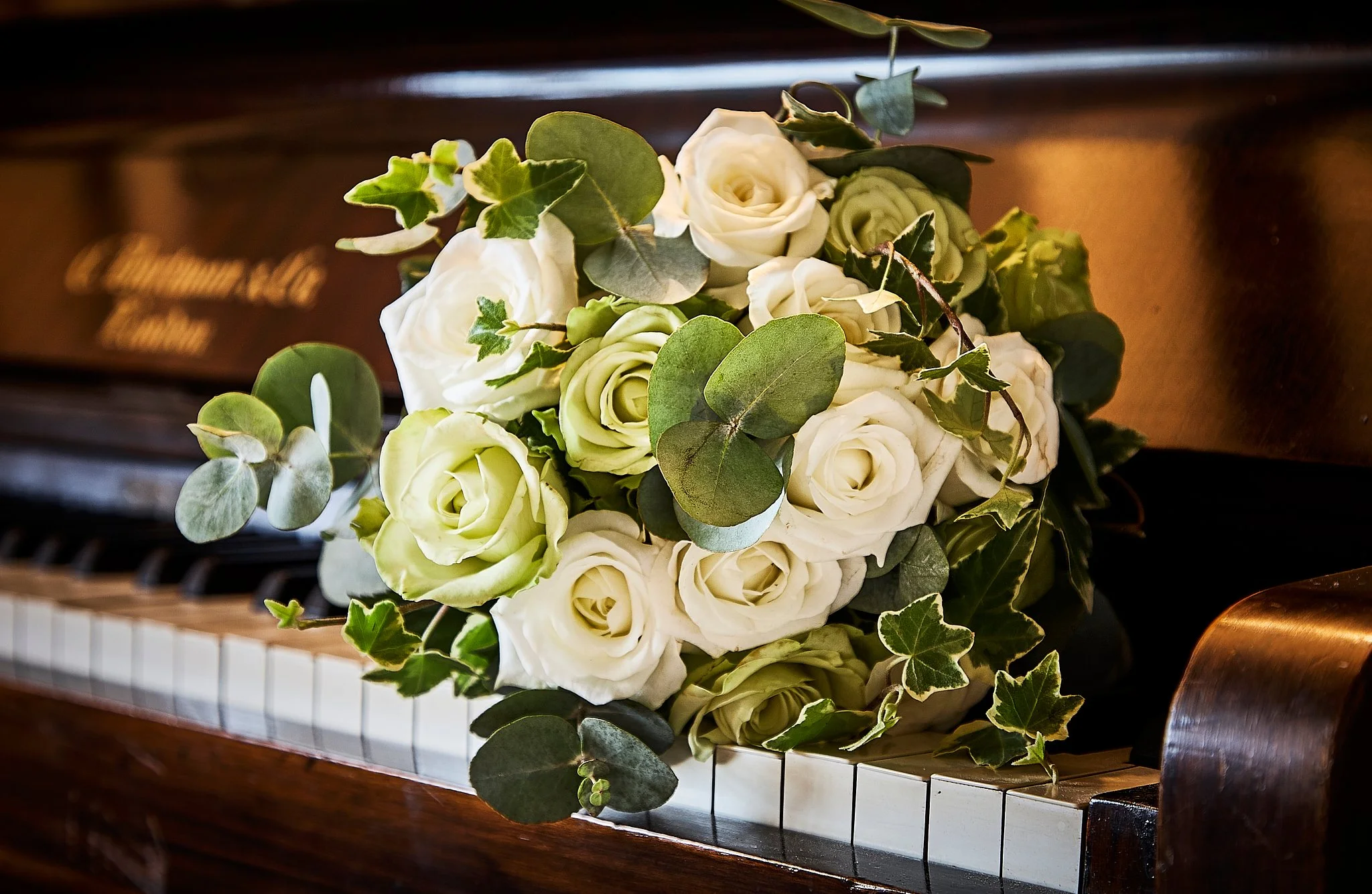 A bouquet of white roses and green leaves resting on a piano with black and white keys.