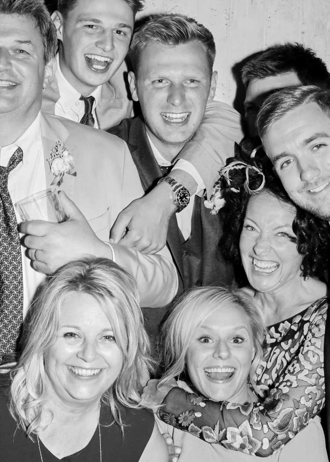 Group of people, mostly young adults and middle-aged, smiling and celebrating, at a social gathering or party, dressed in semi-formal attire, in a wooden interior setting.