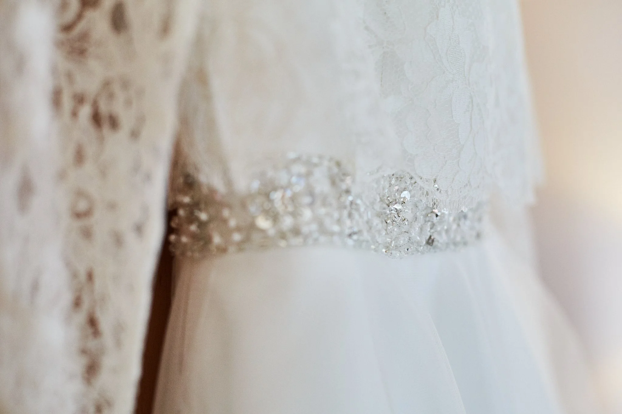 Close-up of lace fabric with small beads and embroidery, possibly part of a wedding dress or elegant garment.