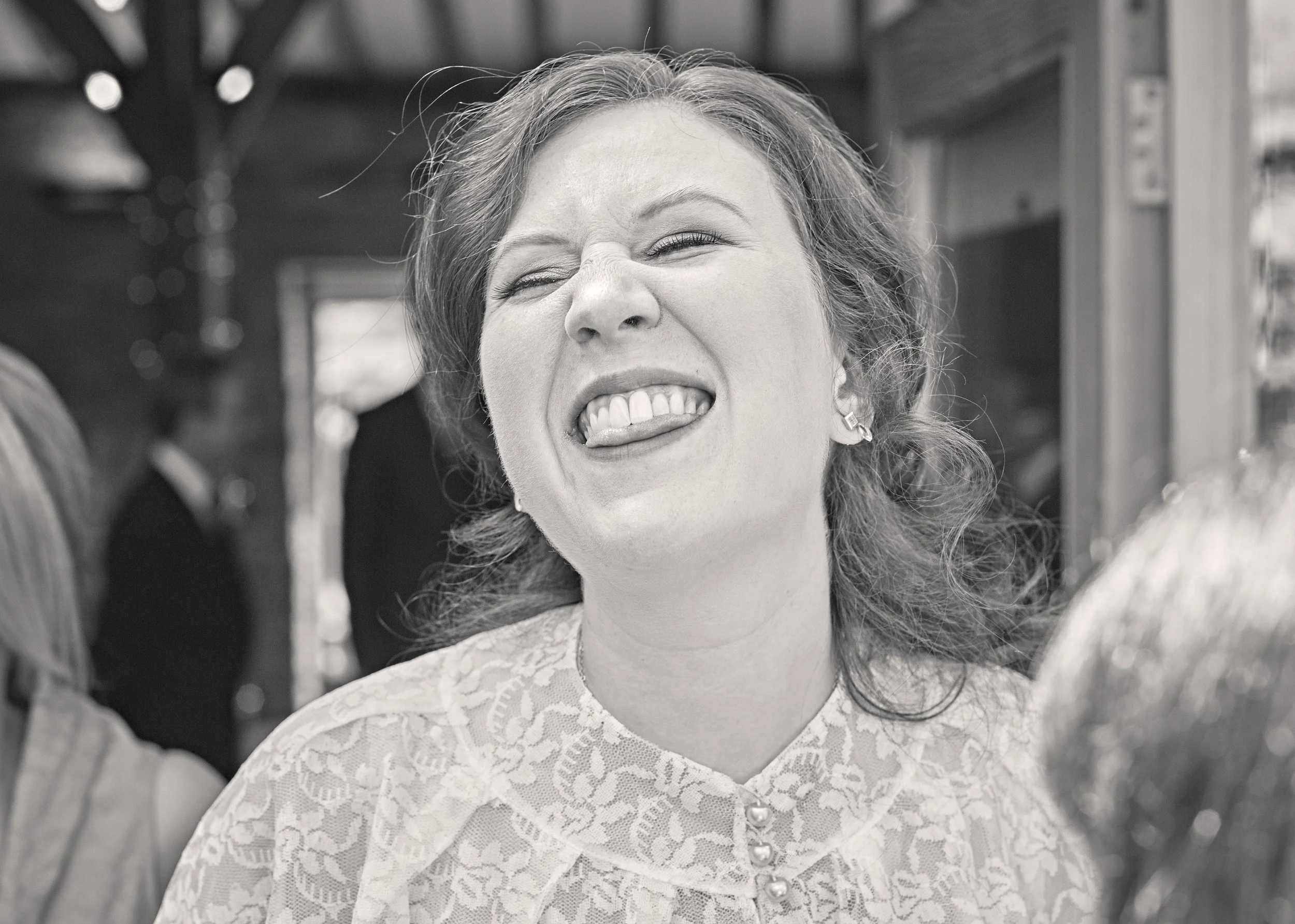 A woman with curly hair smiling with her tongue out, wearing a lace dress, and earrings.