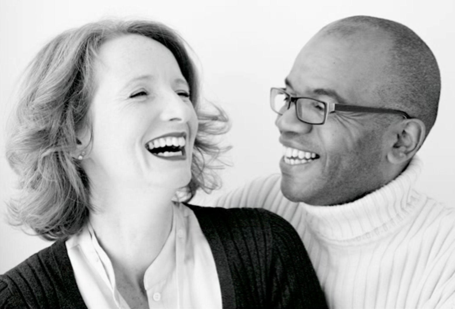 A black-and-white photo of a woman and a man sharing a laugh, facing each other closely.